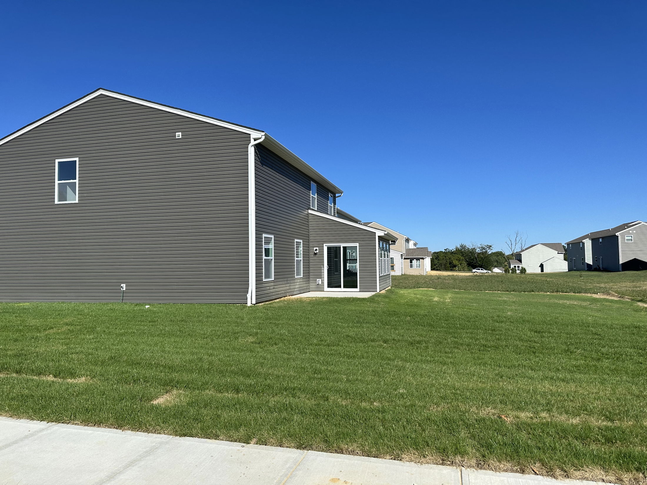 Side view of a modern, two-story grey house with a spacious lawn under a clear blue sky.