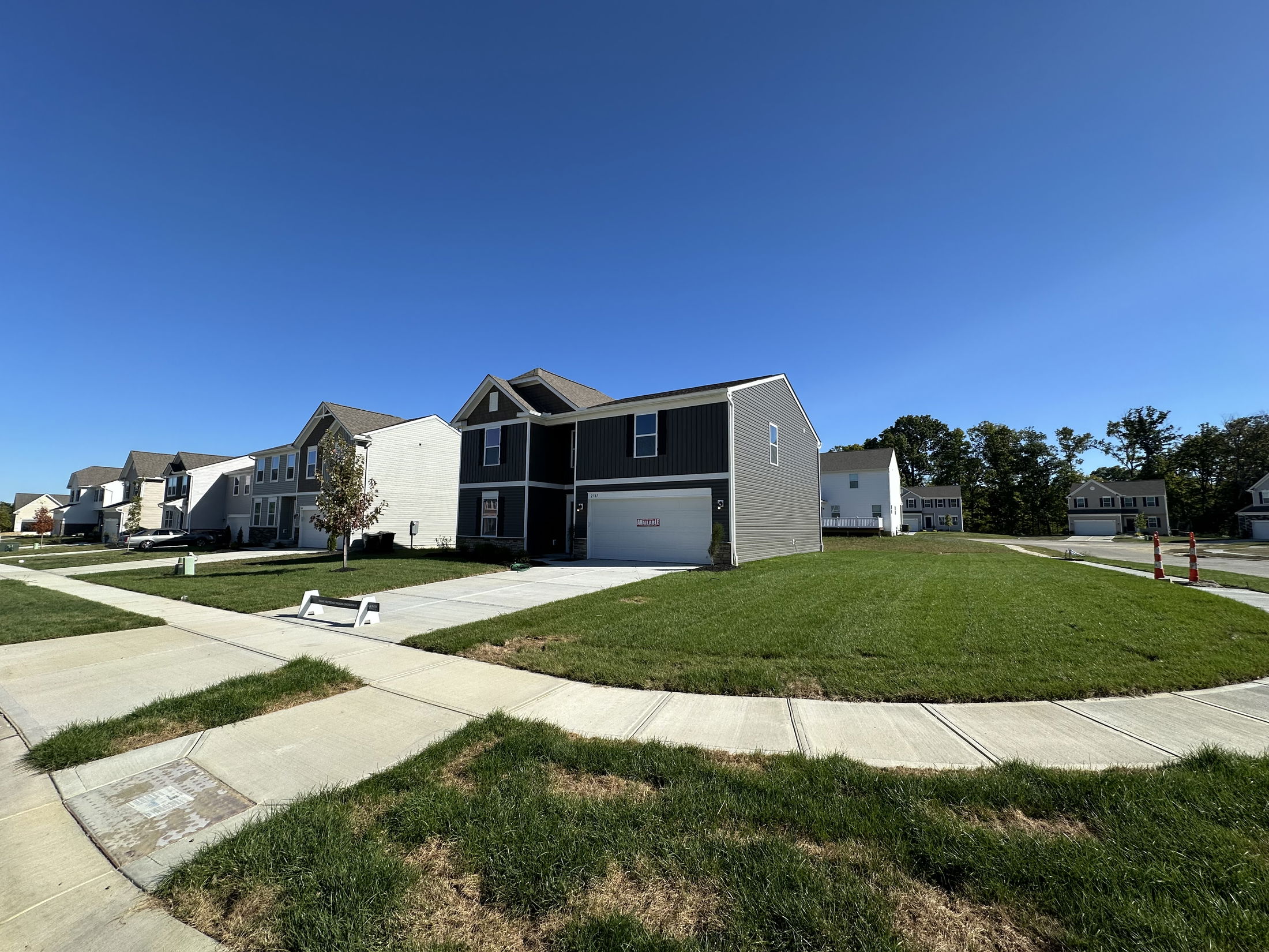 Modern suburban neighborhood with newly built homes, green lawns, and clear blue sky.