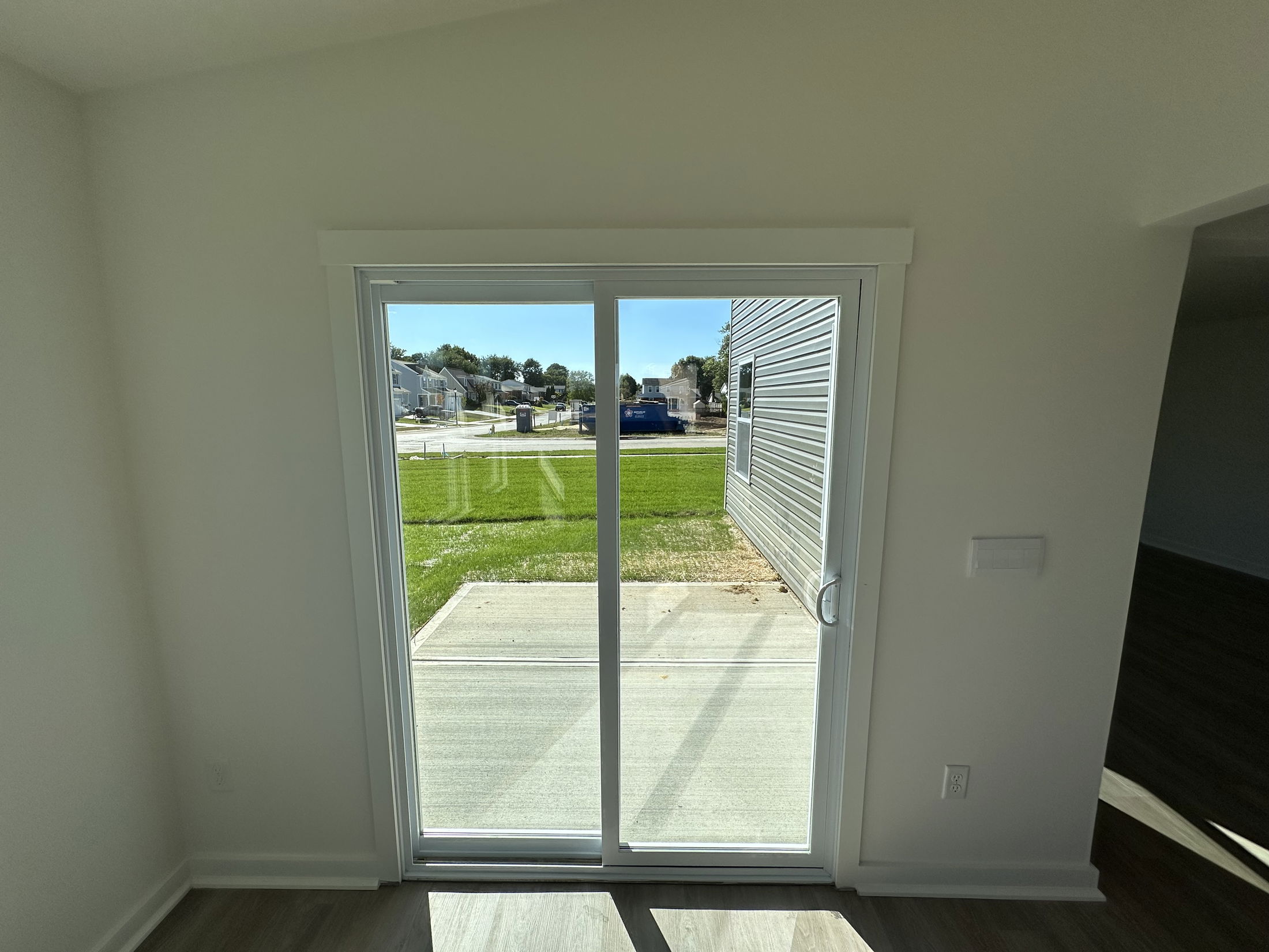 Sliding glass patio door in a modern home interior opening to a sunny backyard with a view of neighboring houses.