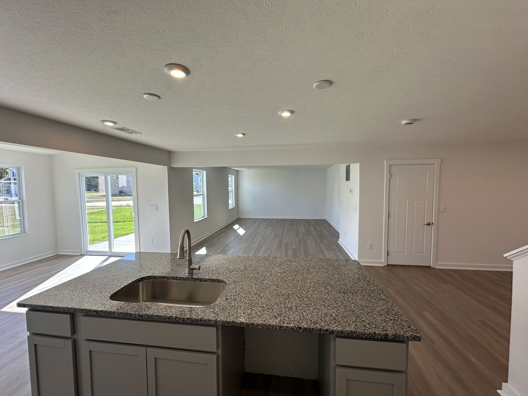Modern open-concept kitchen and living room with granite countertop, beige cabinets, and hardwood floors.