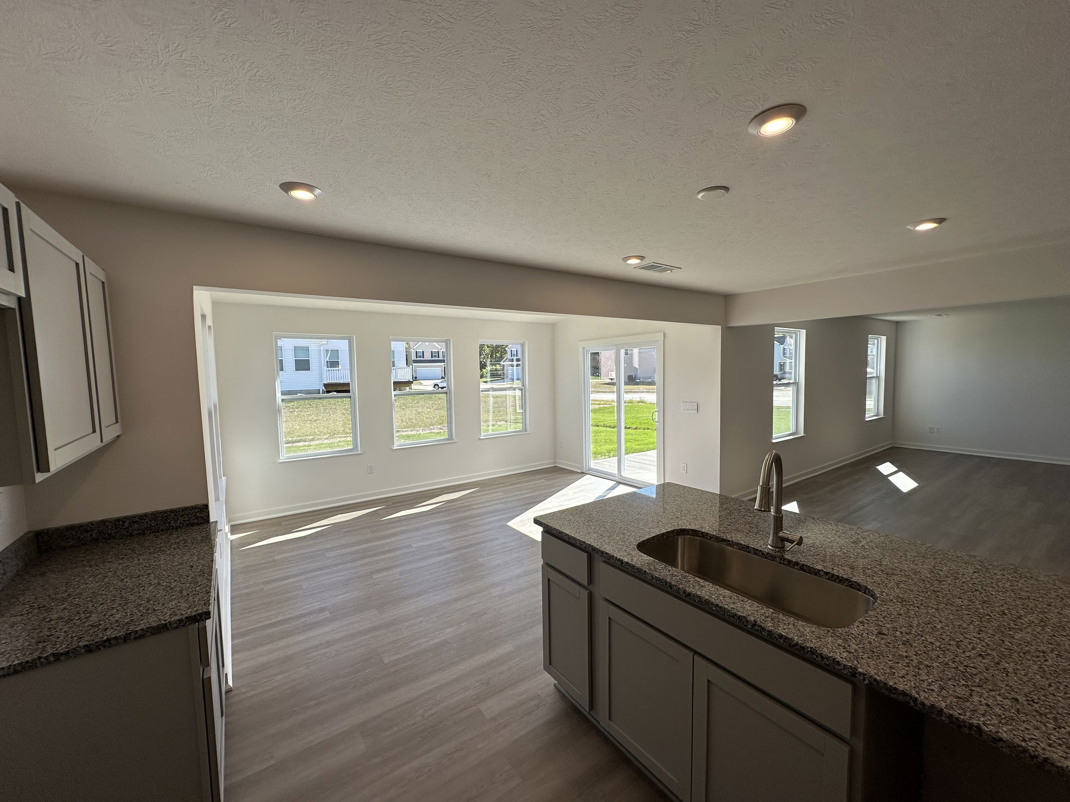 Modern open-concept kitchen and living area with granite countertops and large windows overlooking a green lawn.