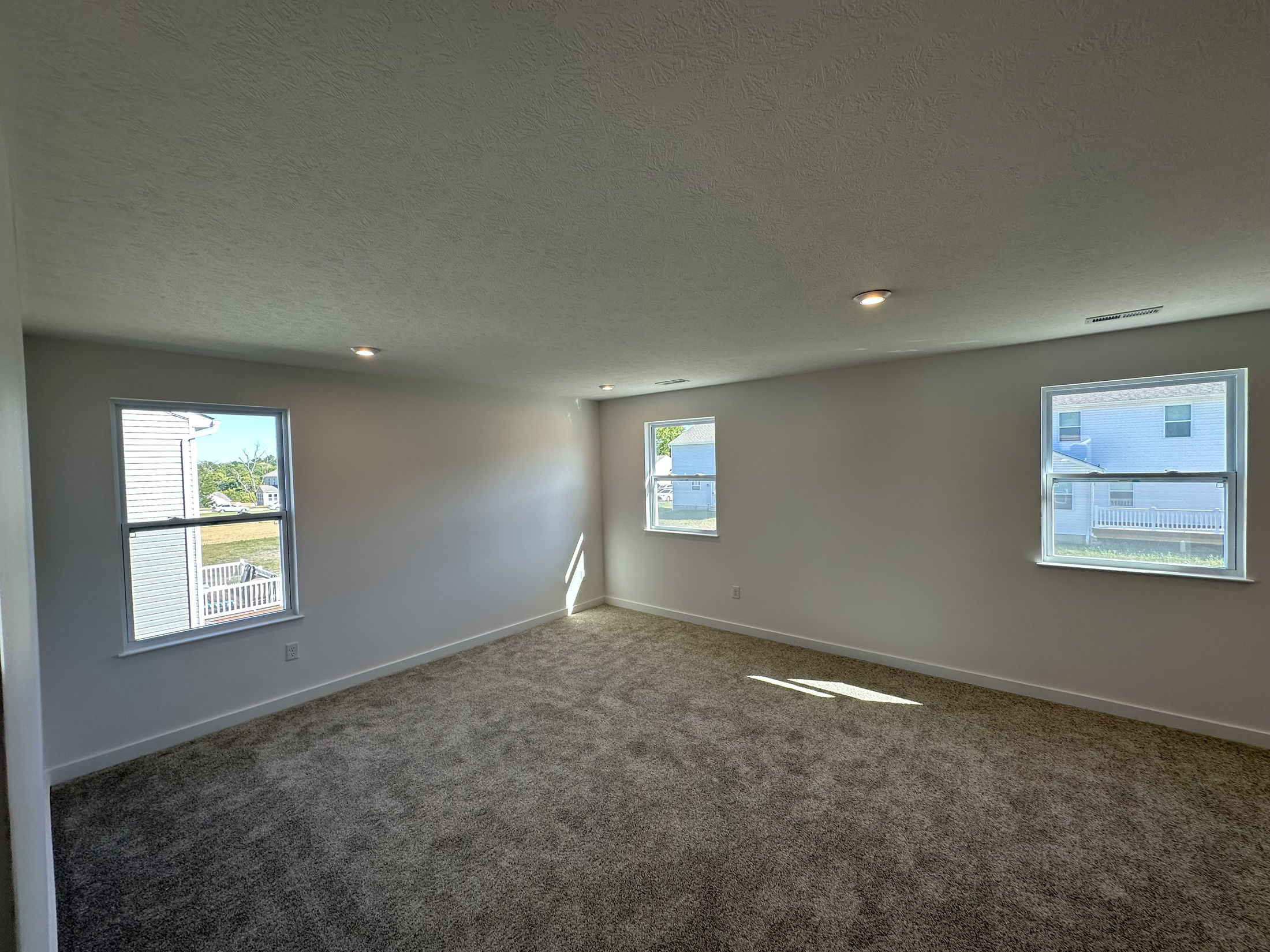 Spacious, carpeted empty room with three windows and recessed lighting.