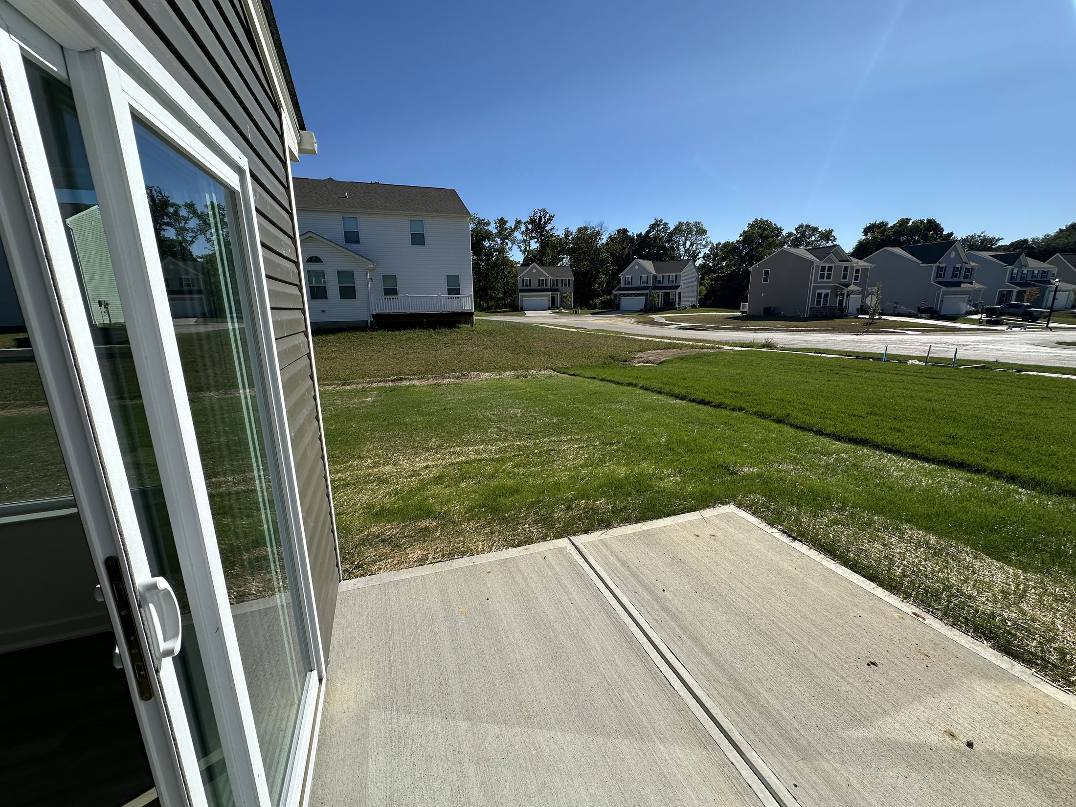 Suburban neighborhood view from a patio door, showing a grassy backyard and several modern houses under a clear blue sky.