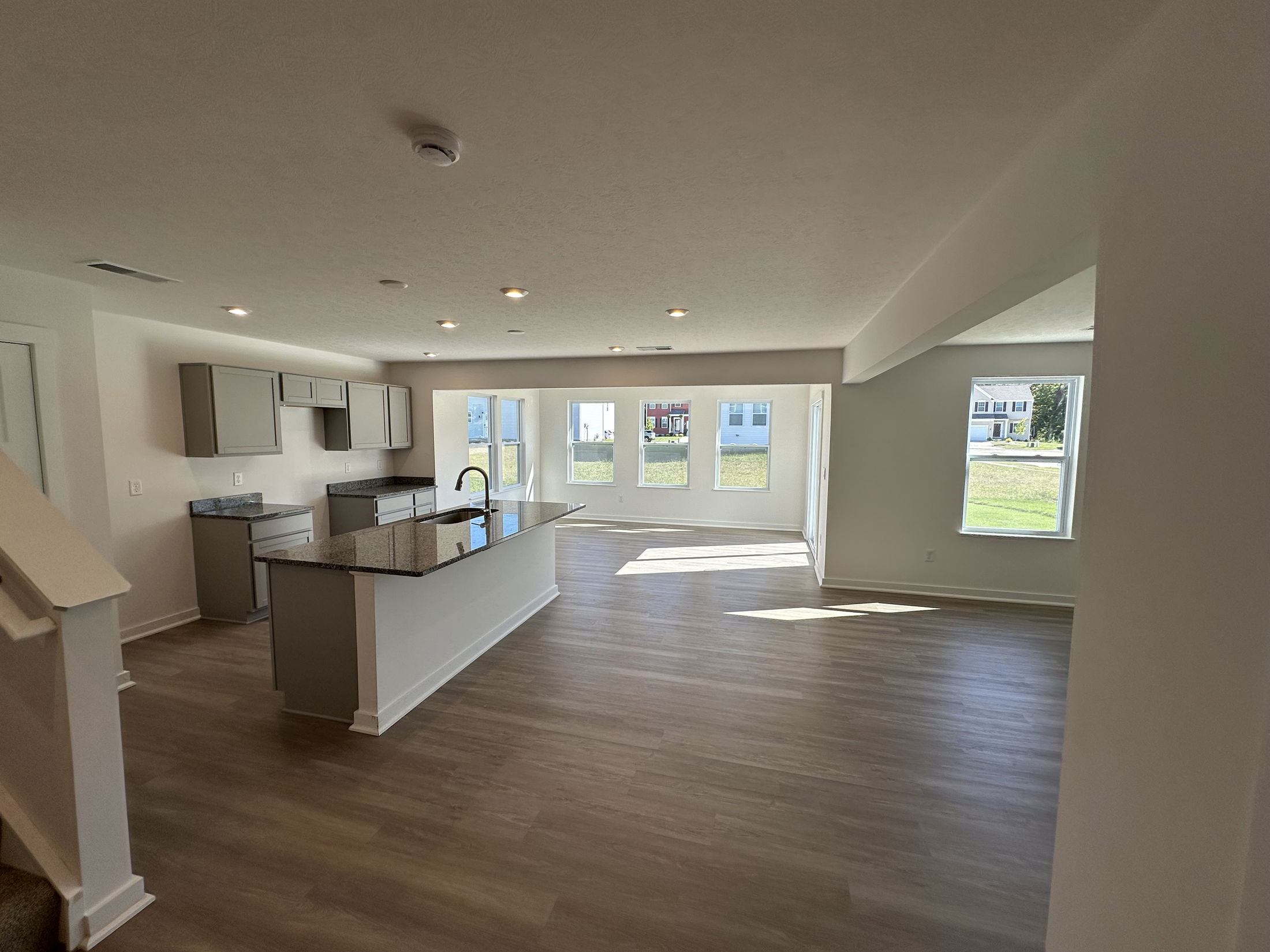 Modern open-concept kitchen and living area with hardwood floors and large windows in a new home.