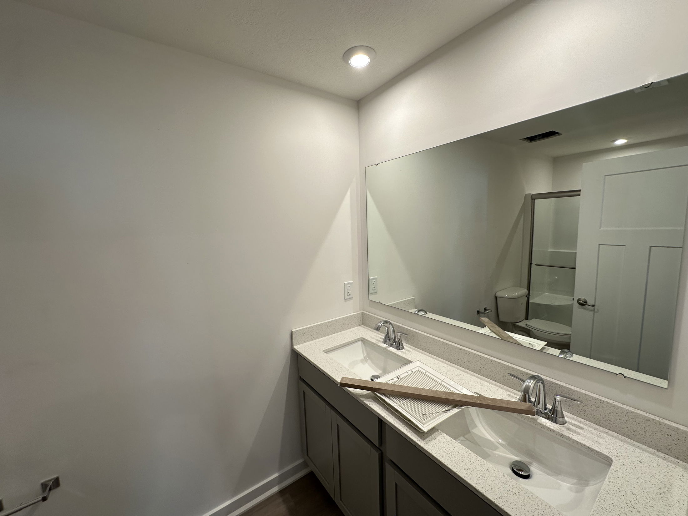 Modern bathroom interior featuring a dual sink vanity, large mirror, and toilet with a shower enclosure in the background.
