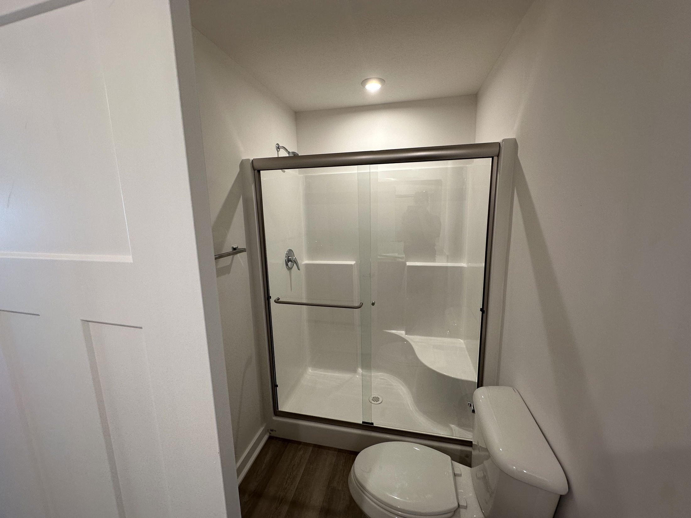 Modern bathroom with glass shower enclosure and white toilet, featuring minimalist design and recessed lighting.