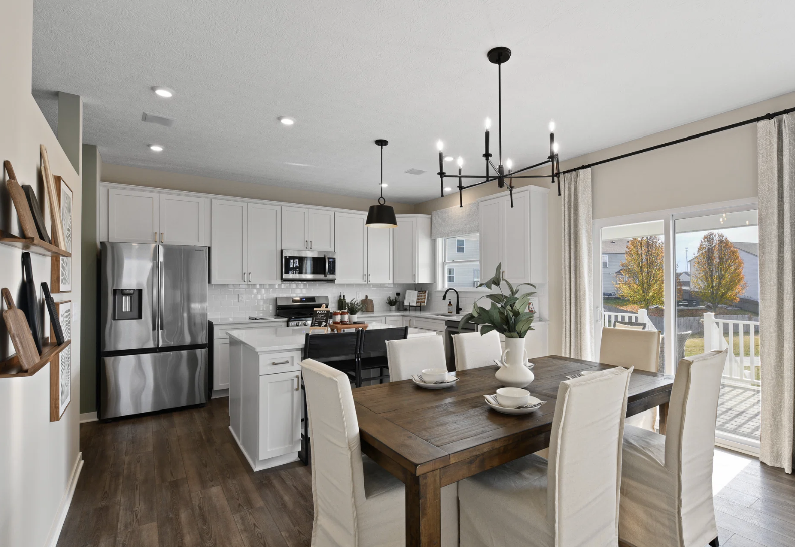 Modern kitchen with white cabinetry, stainless steel appliances, and a wooden dining table set for six, featuring large windows that let in natural light.
