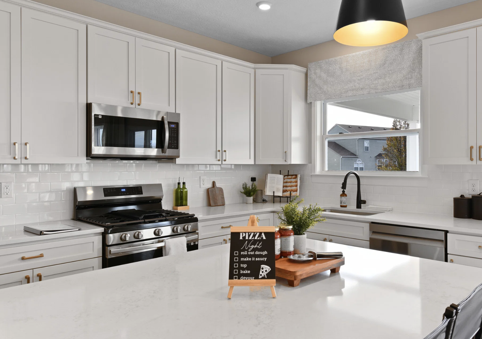 Modern kitchen featuring white cabinetry, stainless steel appliances, and a marble countertop with a menu board displaying pizza options.