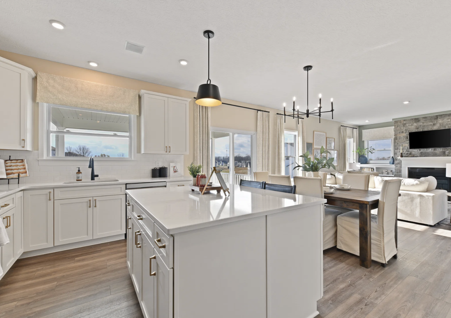 Bright modern kitchen with white cabinets, a large island, and a dining area featuring a stylish chandelier and a view of a living room.