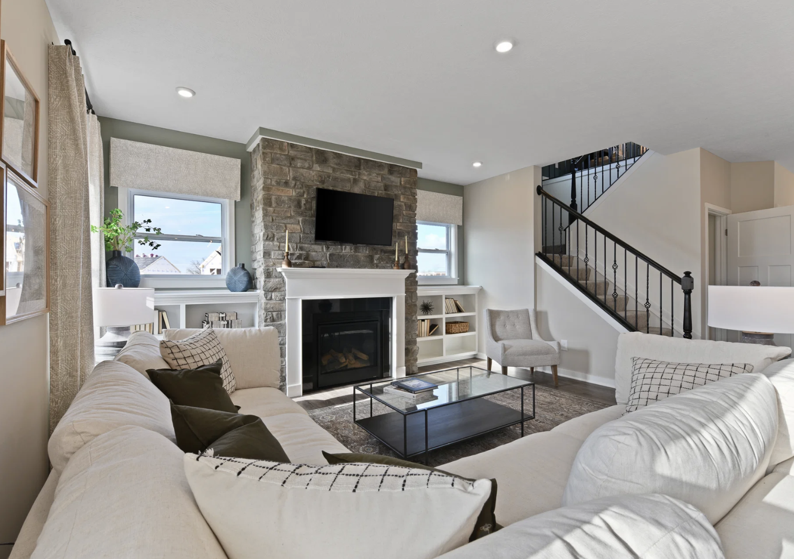 A modern living room featuring a stone fireplace, a large sectional sofa, a glass coffee table, and natural light from windows.