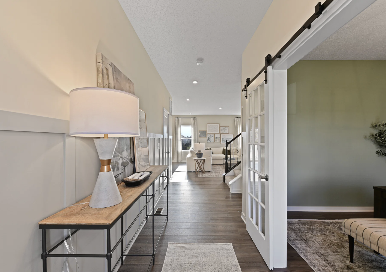 A hallway with a wooden console table, a lamp, and a sliding glass door leading to a living area.