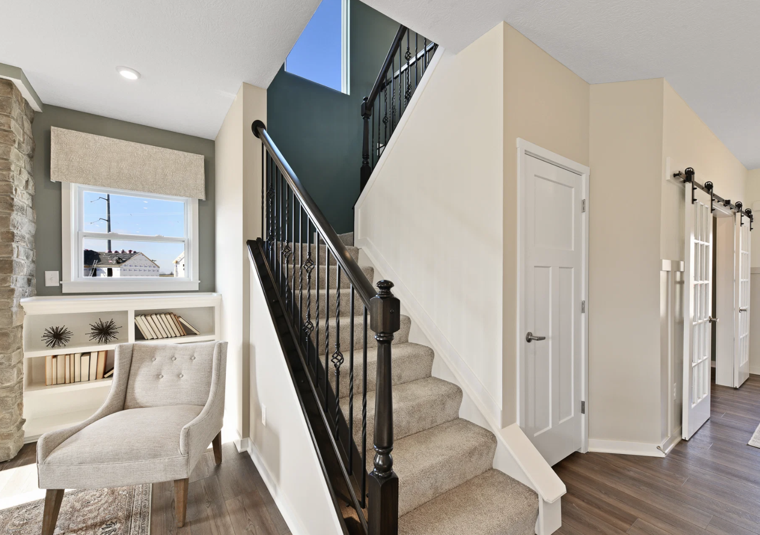 A bright interior featuring a staircase, a chair, and a doorway leading to another room.