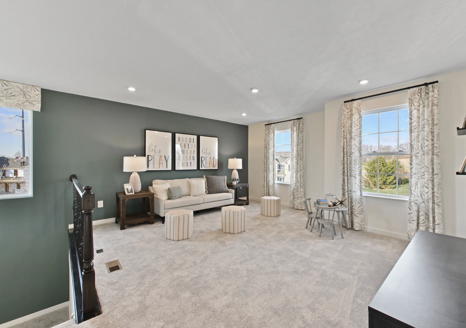 A cozy living space with a sofa, decorative pillows, two small stools, and large windows overlooking greenery.