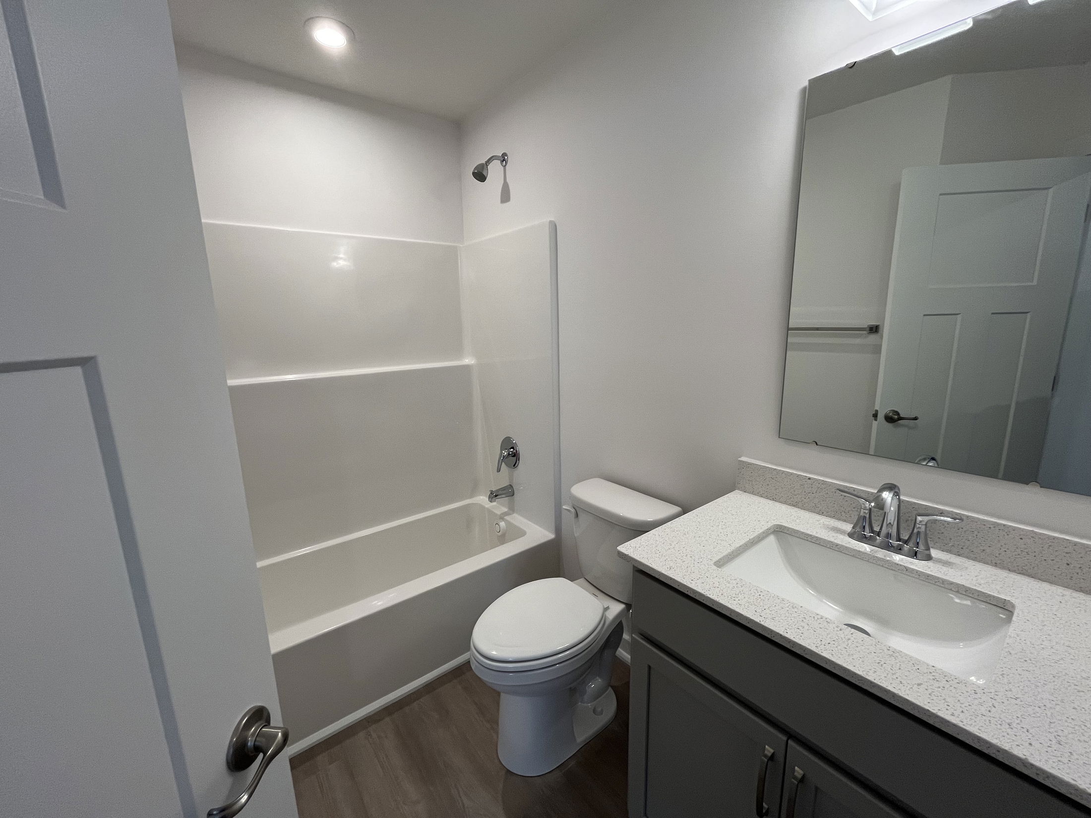 Modern white bathroom with a bathtub, toilet, and a sink vanity featuring a large mirror and sleek fixtures.
