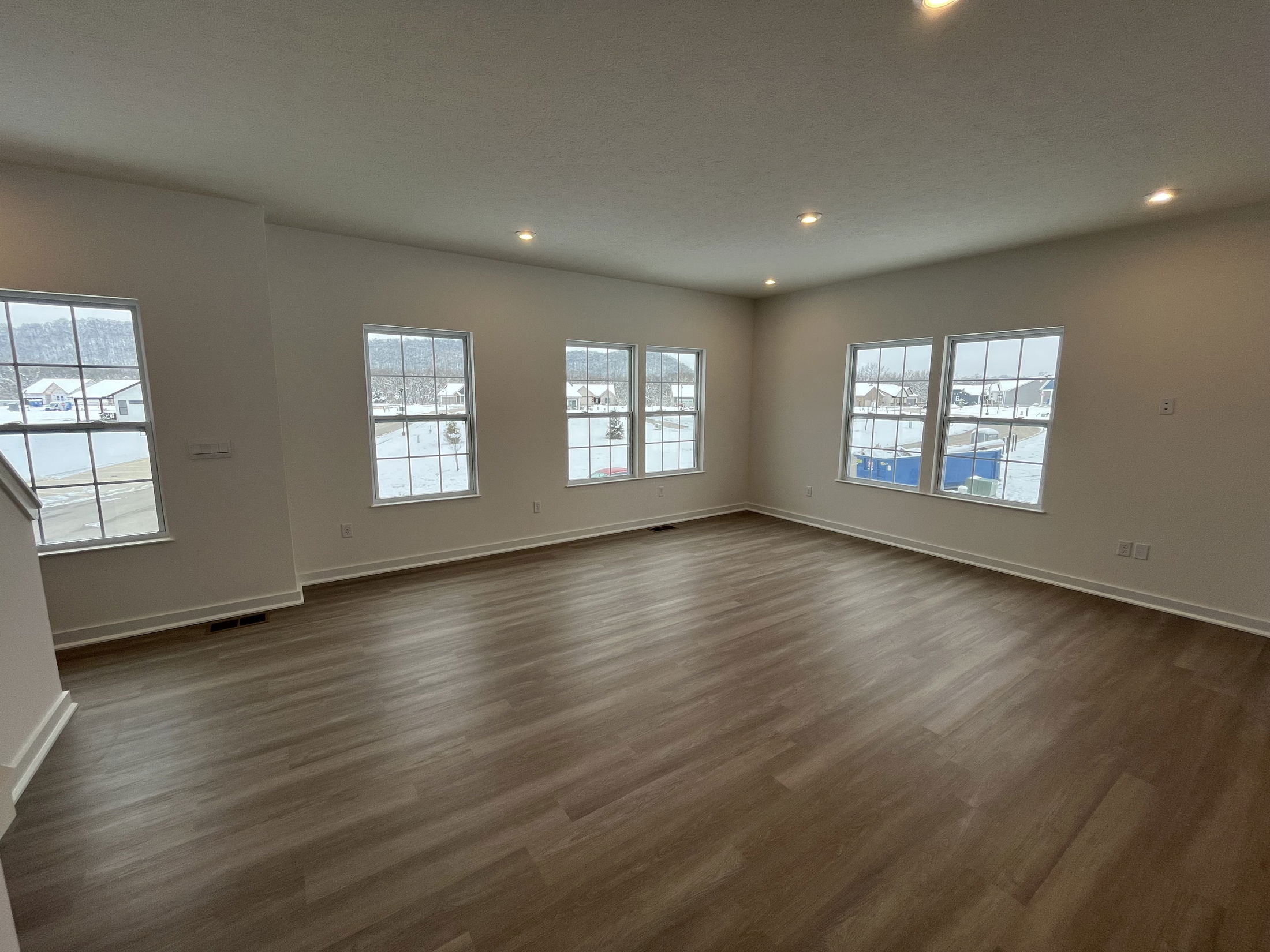 Modern empty room with large windows and light wood flooring offering a spacious, well-lit interior view.