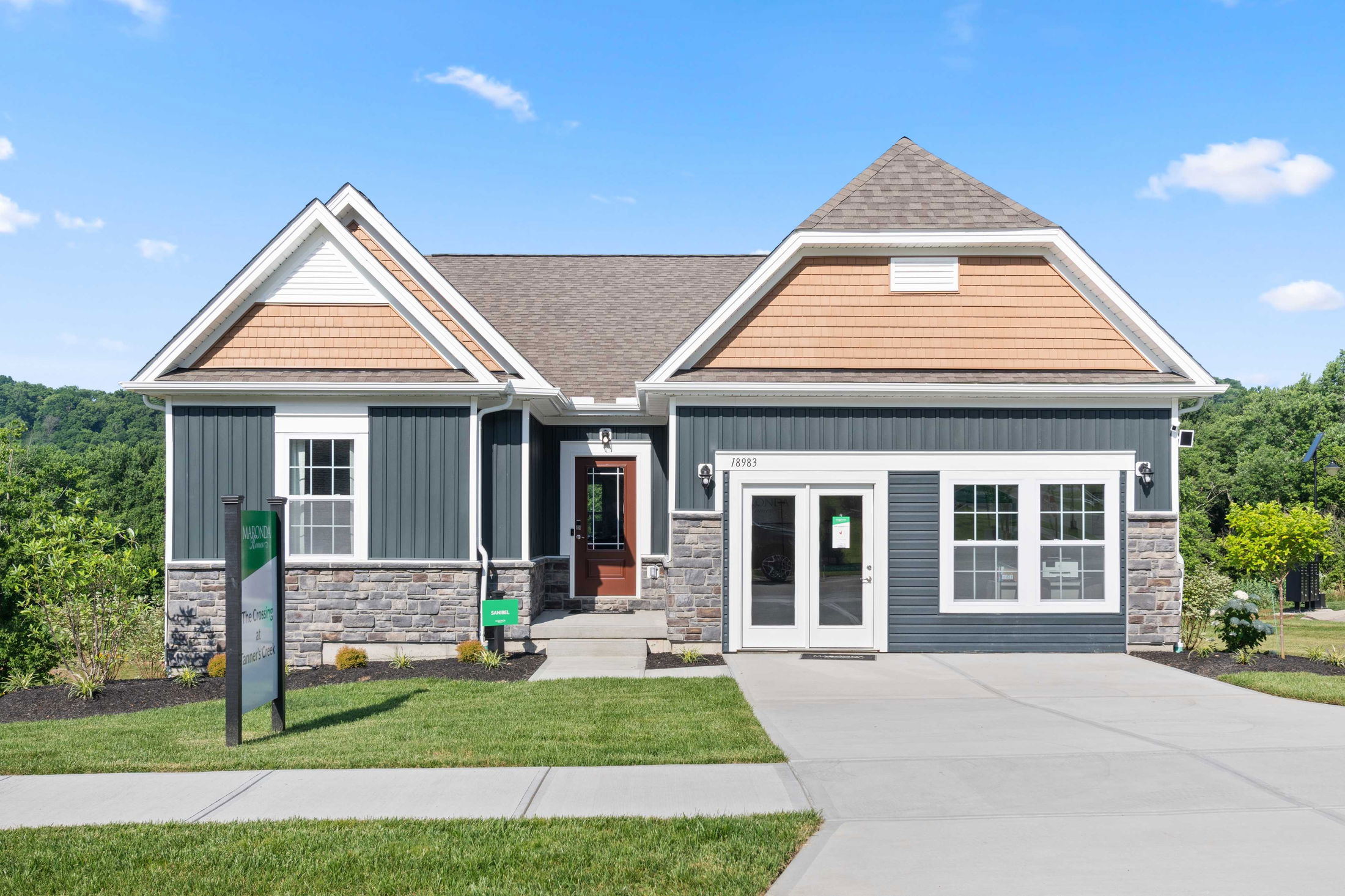 Modern suburban house with gray siding, stone accents, and driveway under a clear blue sky.