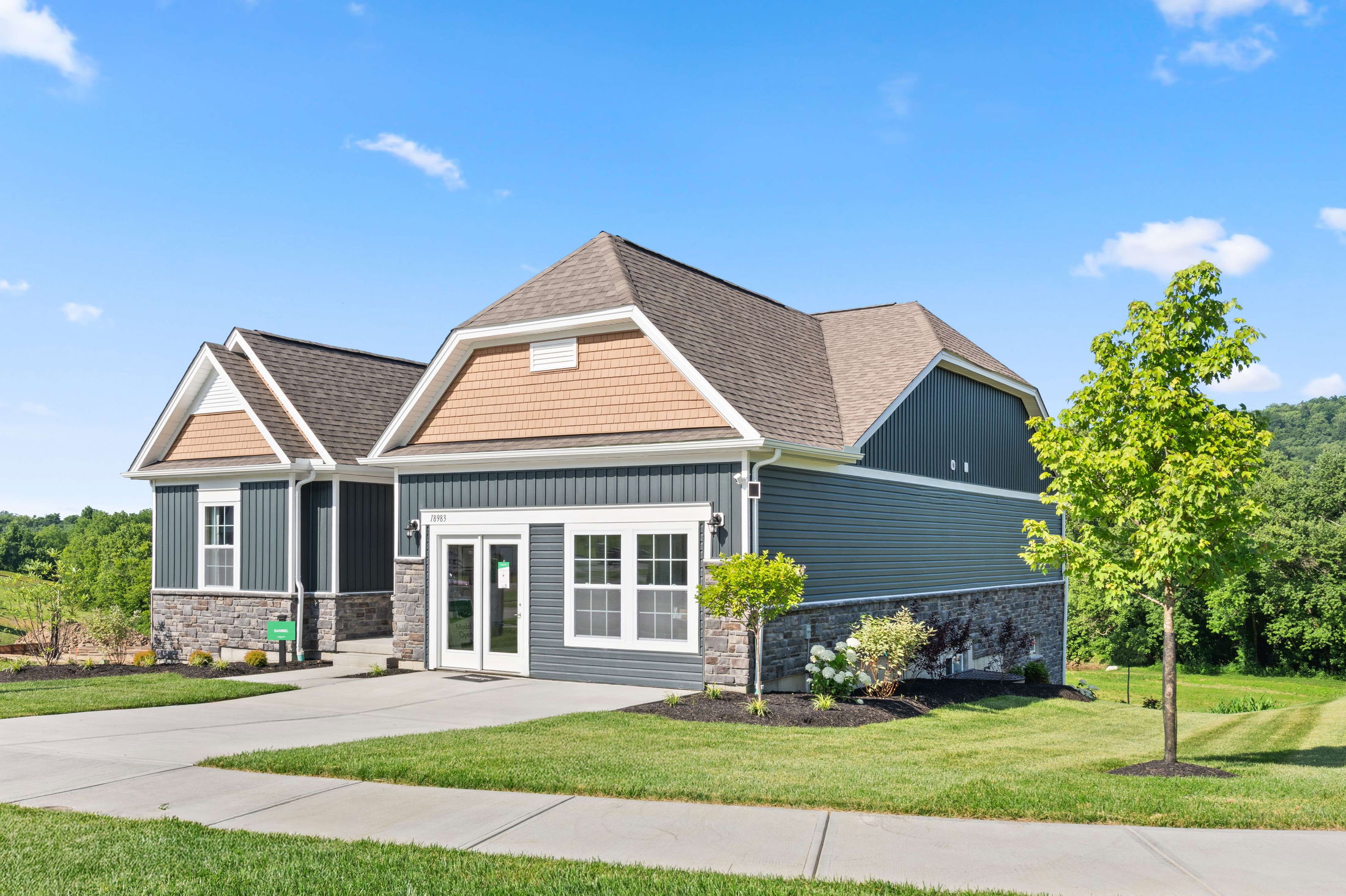Modern suburban house with beige and blue siding, surrounded by a well-maintained lawn and clear blue sky.