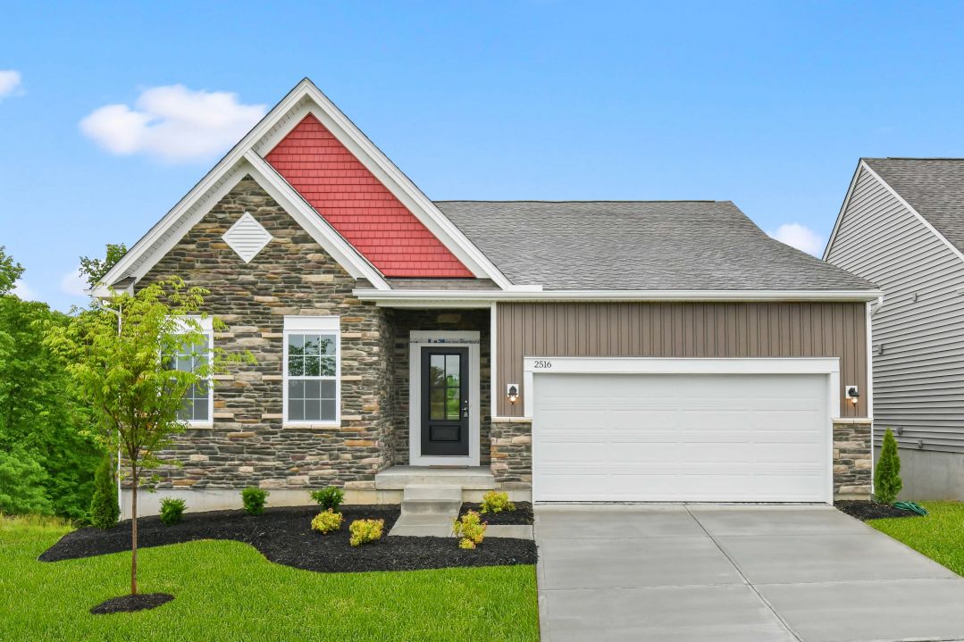 Front view of a modern, single-story house with stone and red siding exterior, a two-car garage, and landscaped yard.