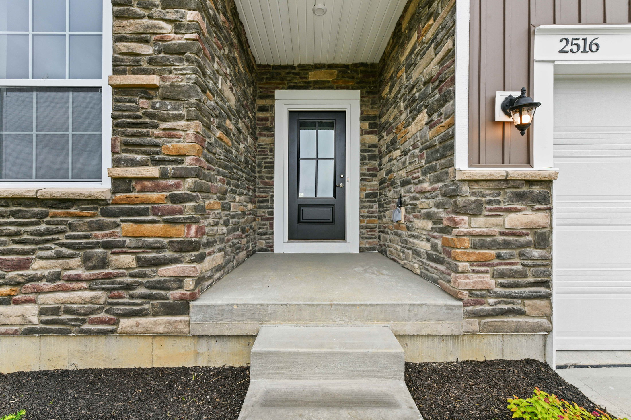 Front entrance of a modern home with stone facade, black door, and outdoor light fixture.