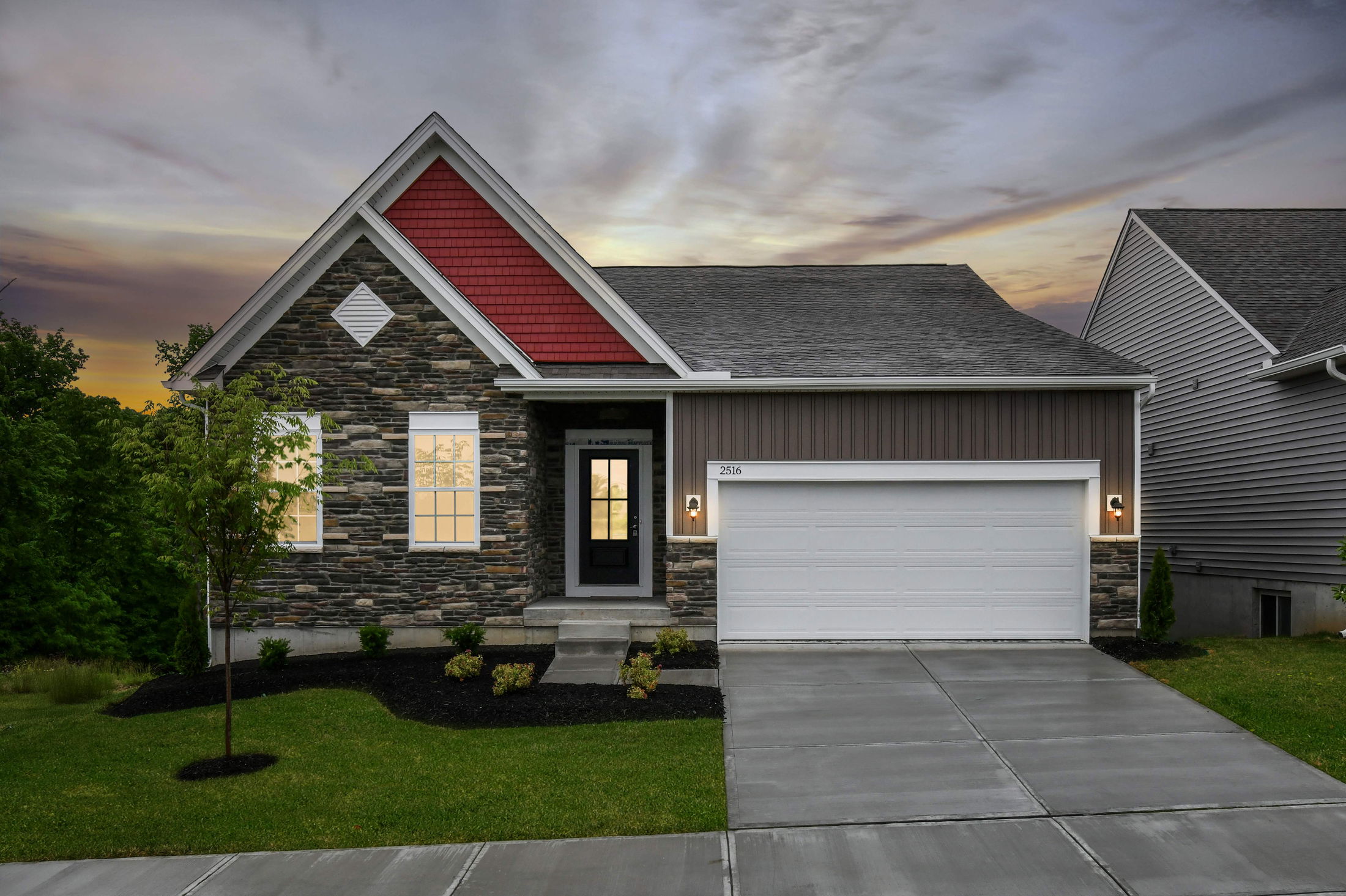 Modern suburban house with stone facade, red accents, and a two-car garage during sunset.