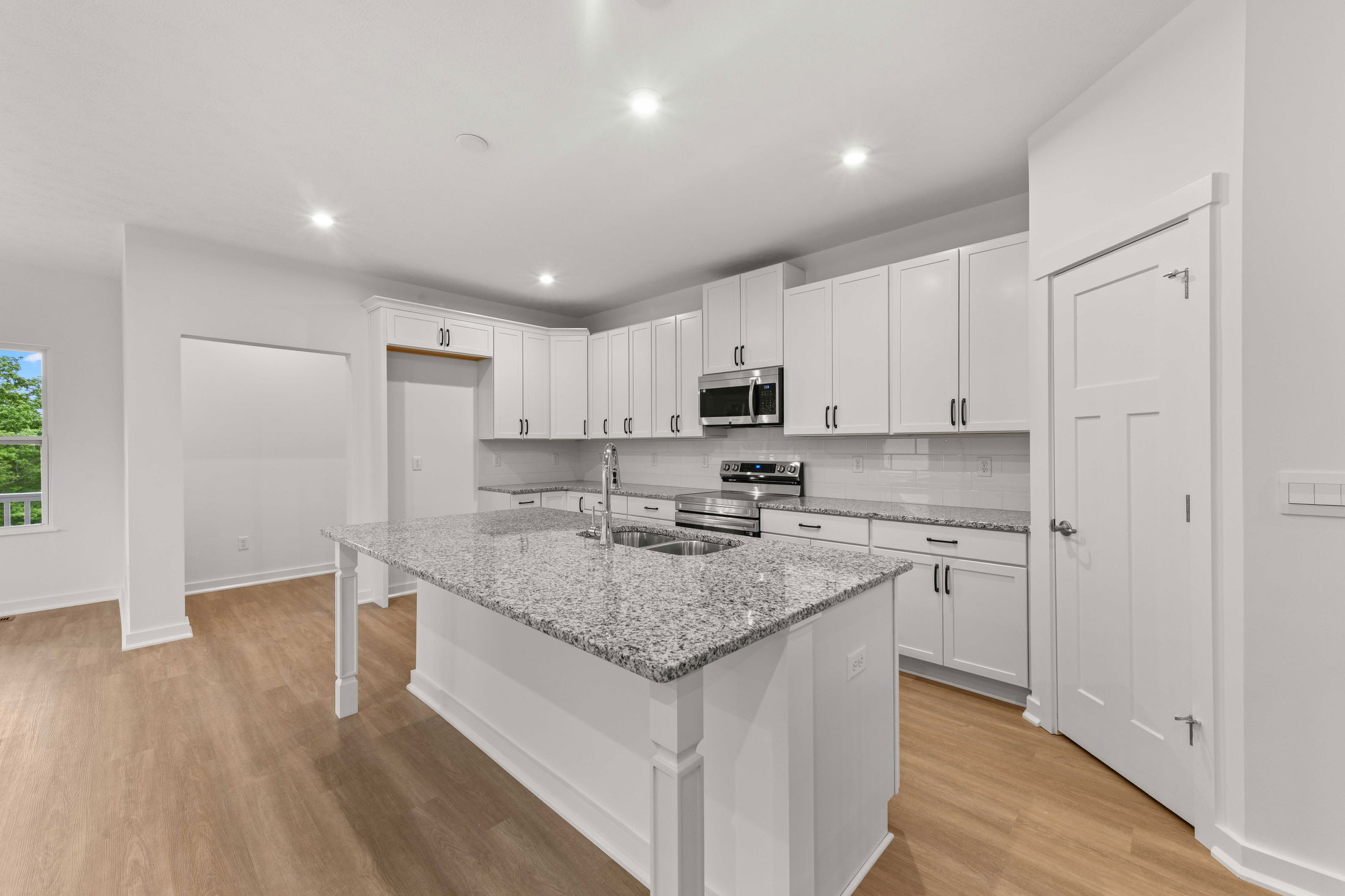 Modern kitchen with granite countertops, white cabinets, stainless steel appliances, and wooden flooring.
