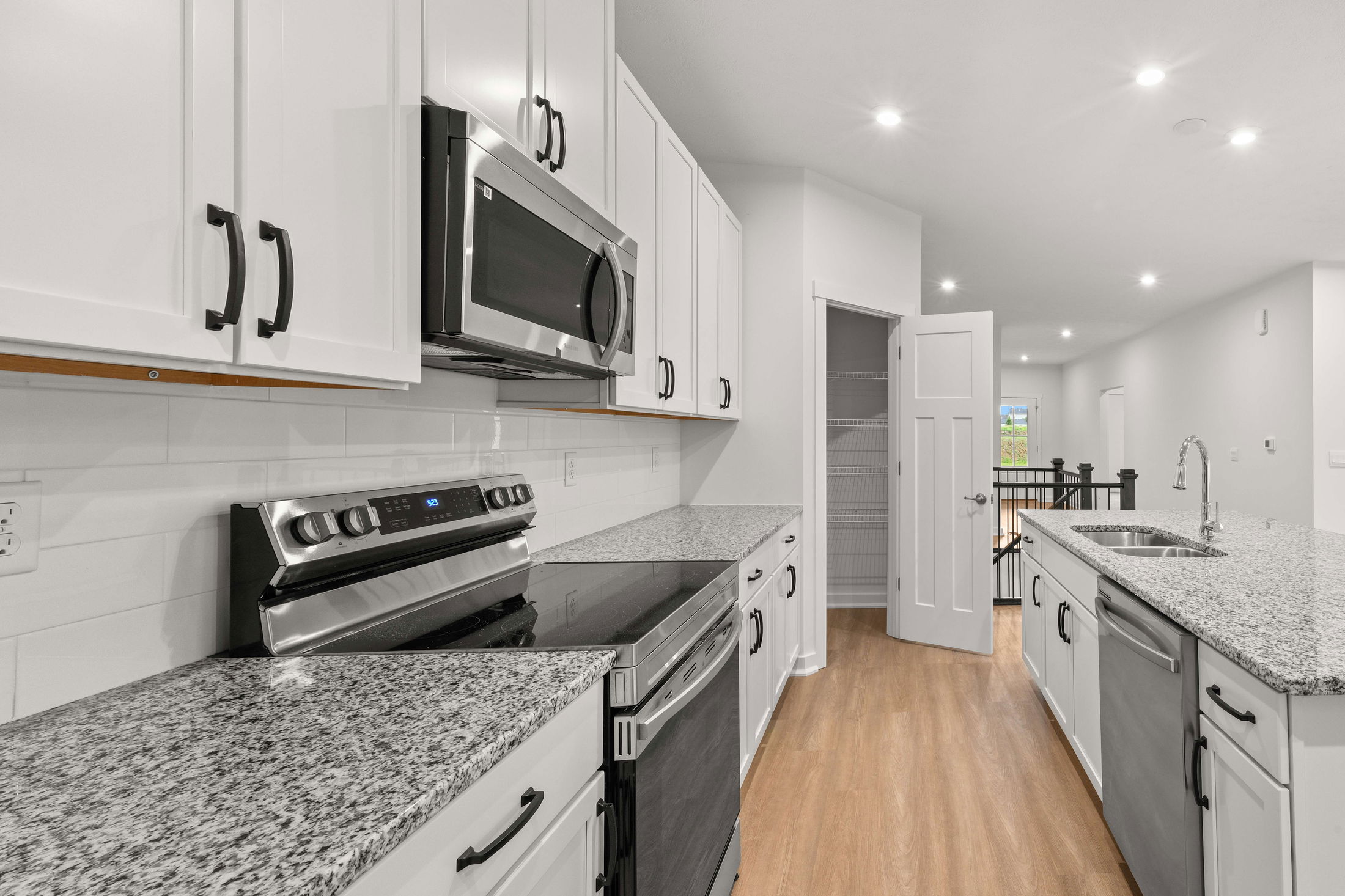 Modern kitchen with stainless steel appliances, granite countertops, white cabinets, and wood flooring.