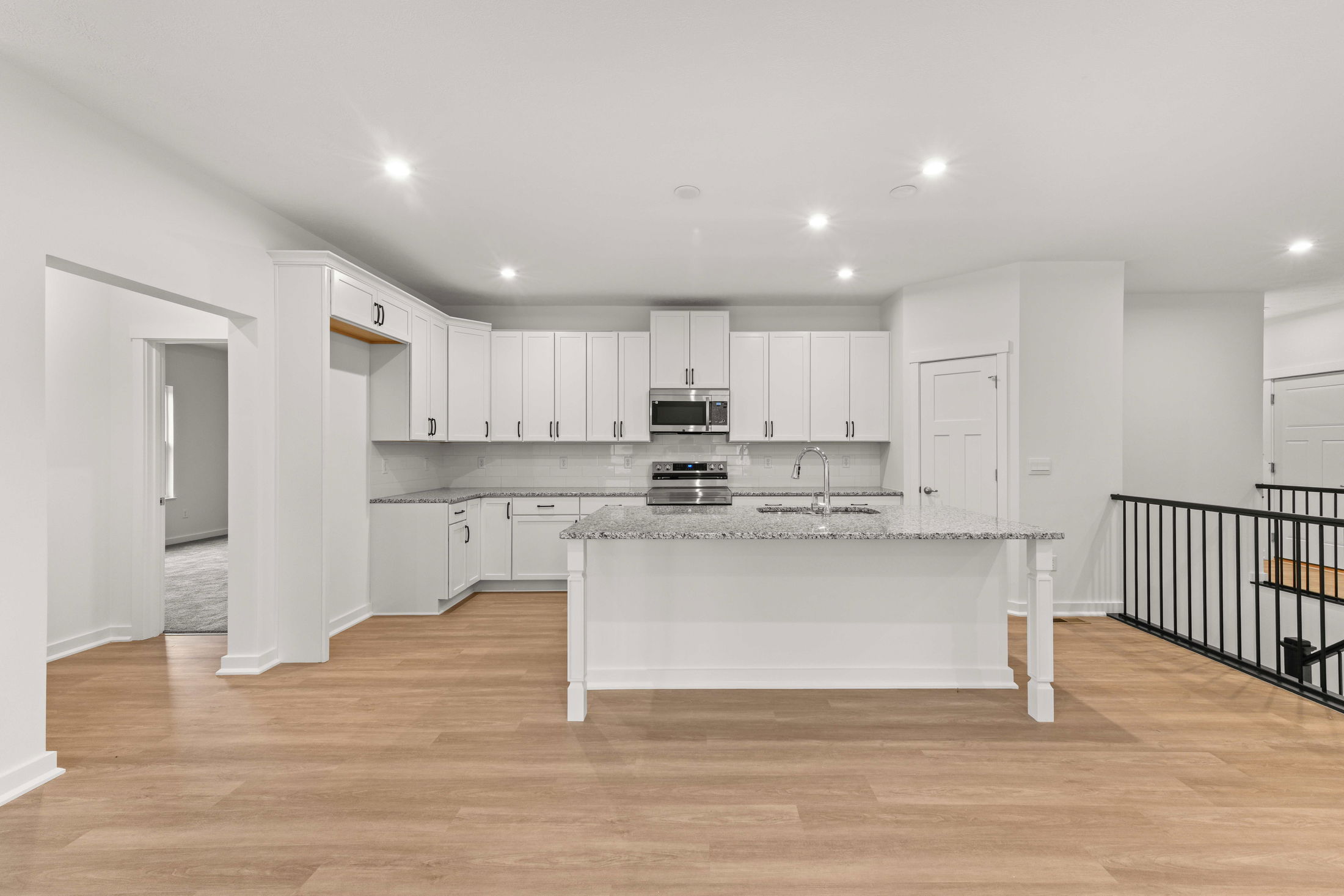 Modern kitchen with white cabinets, granite countertops, and stainless steel appliances in an open-concept layout.
