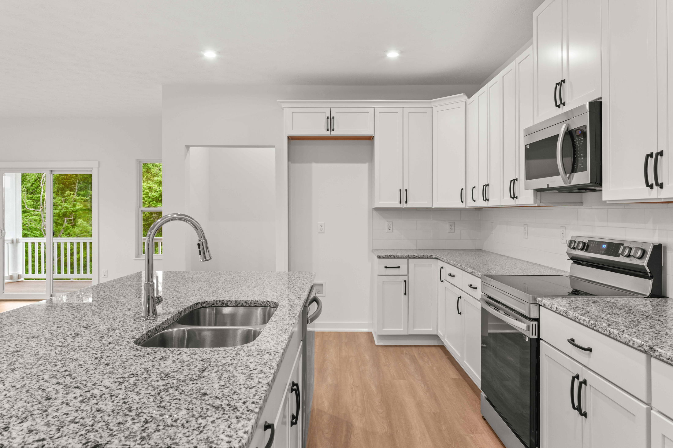 Sleek modern kitchen with white cabinets, granite countertops, stainless steel appliances, and wood flooring.