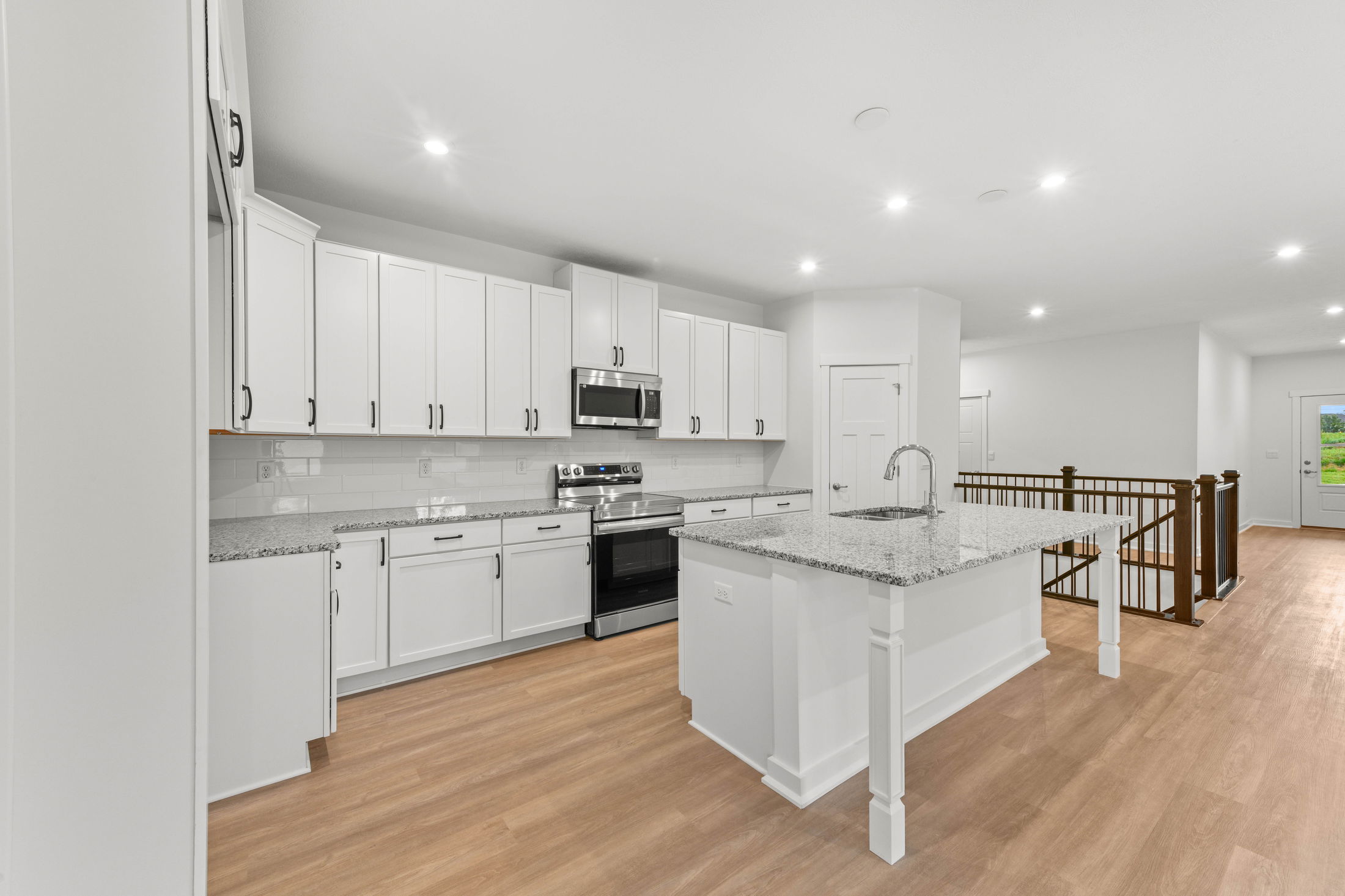 Modern kitchen with white cabinetry, granite countertops, stainless steel appliances, and hardwood flooring.