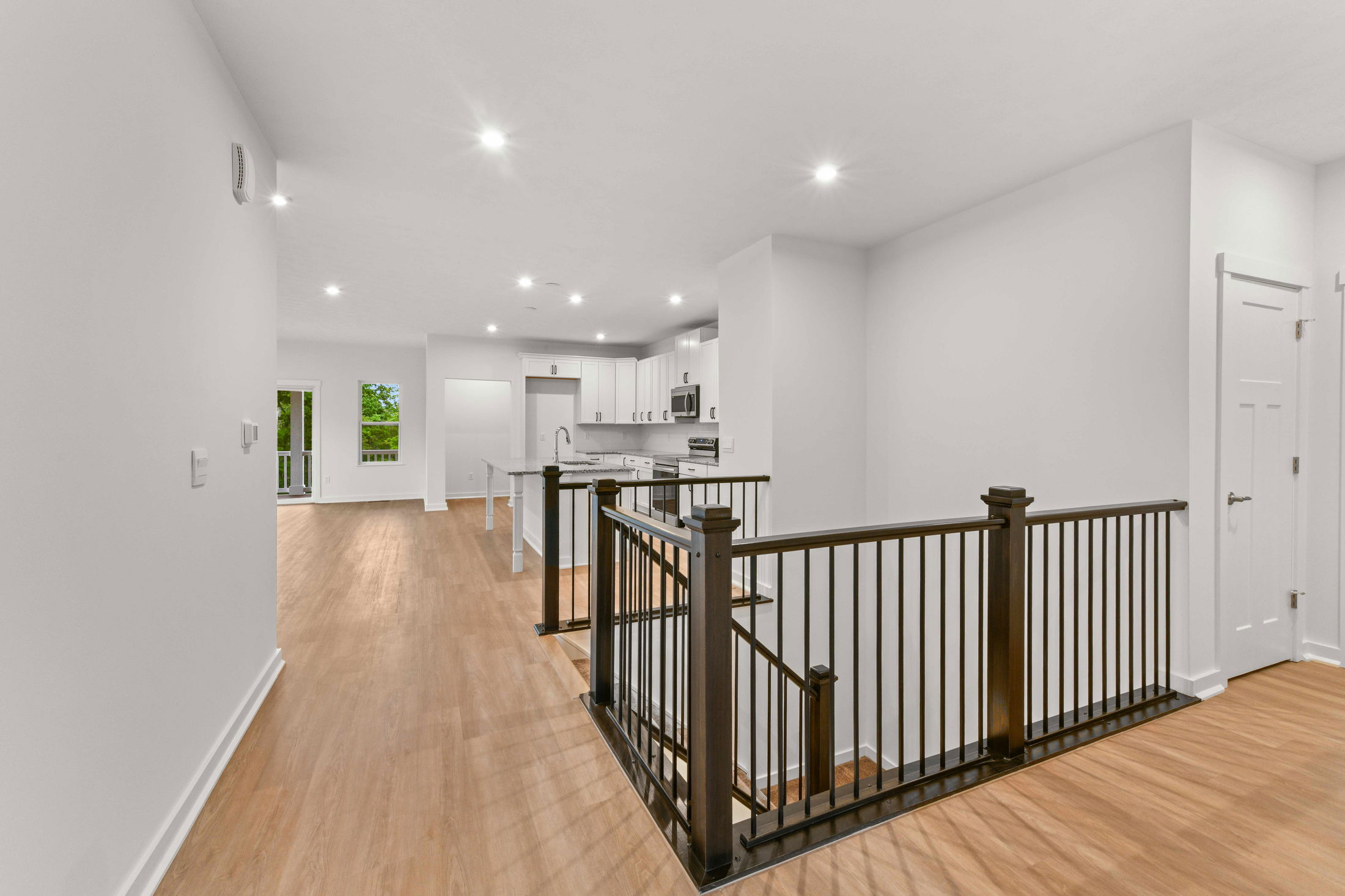 Modern open-concept kitchen and living space with white cabinetry, granite countertops, wooden flooring, and recessed lighting.
