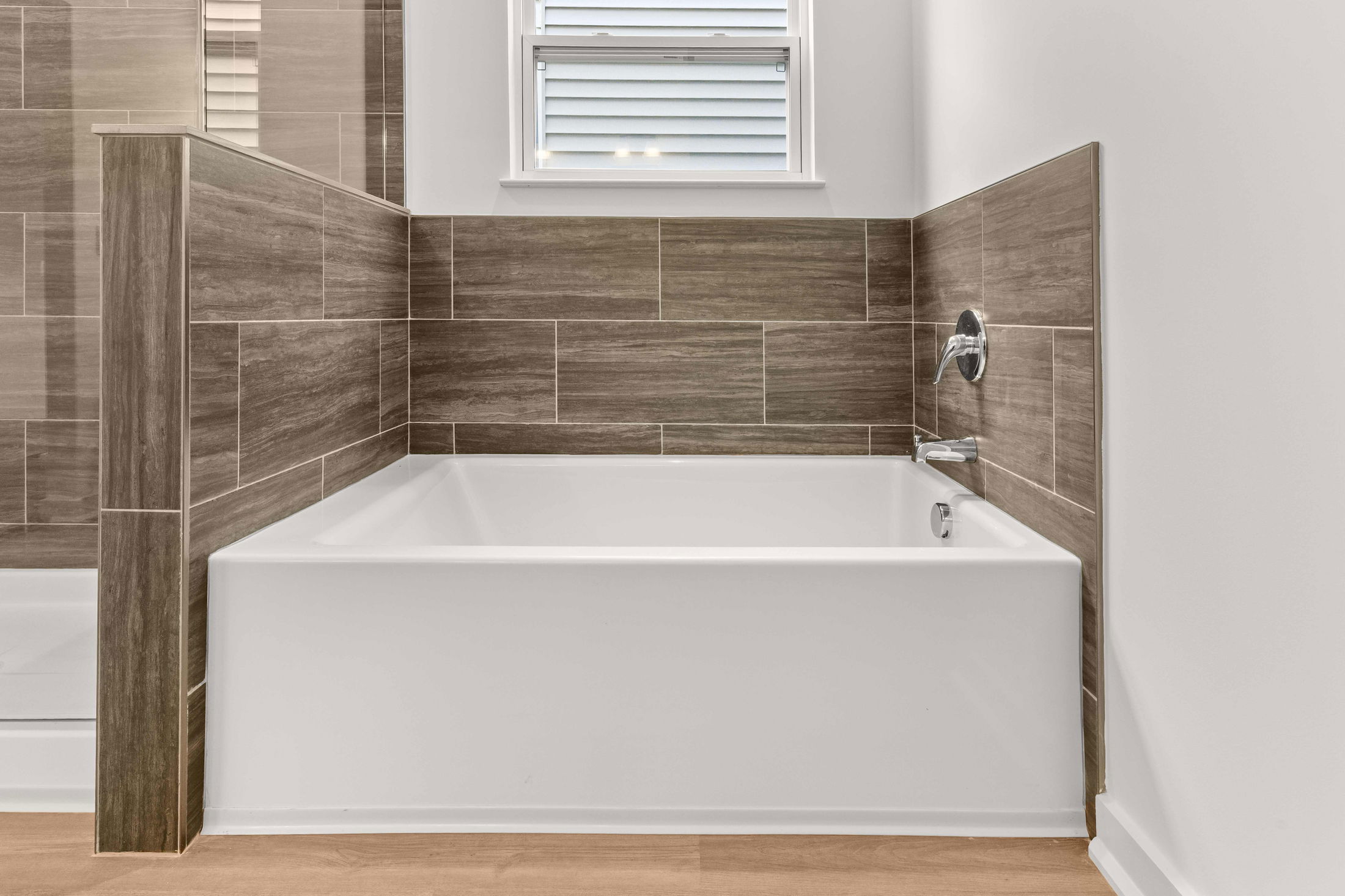Modern bathroom featuring a white bathtub with brown tile backsplash and chrome fixtures.