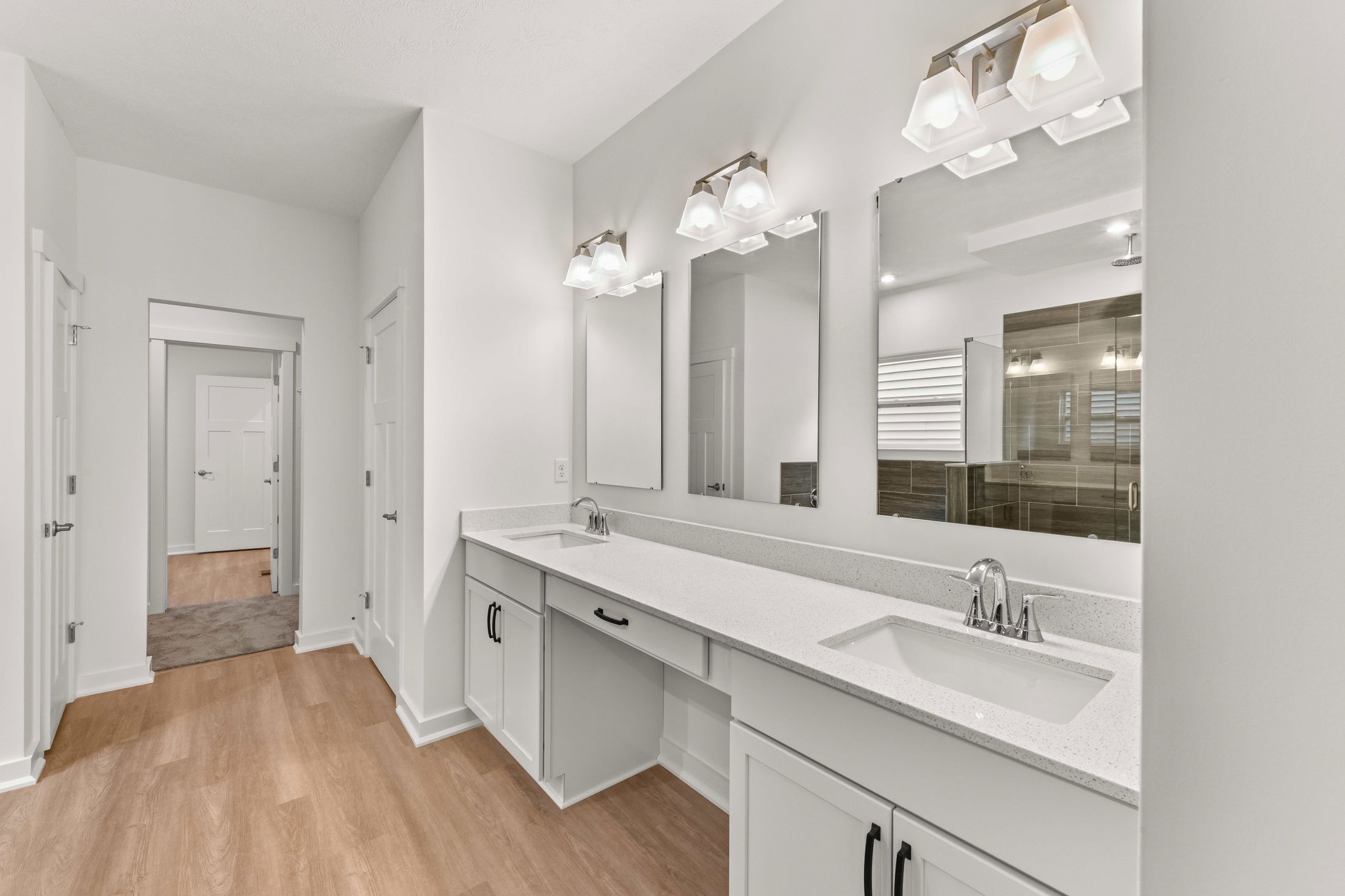Modern bathroom interior with dual sinks, large mirrors, white cabinets, and wood flooring.