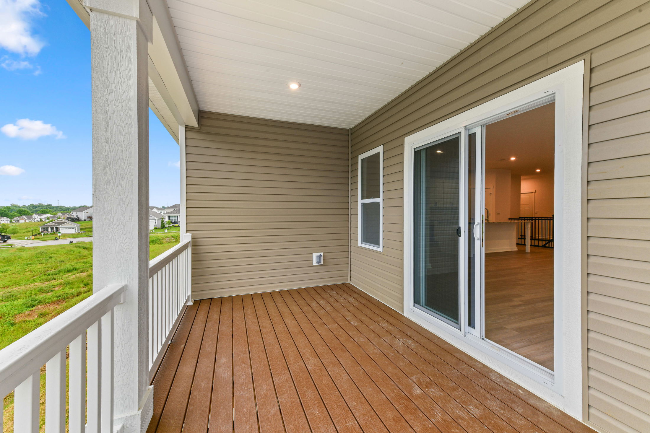 Covered balcony with wooden decking and sliding glass doors overlooking a suburban neighborhood.