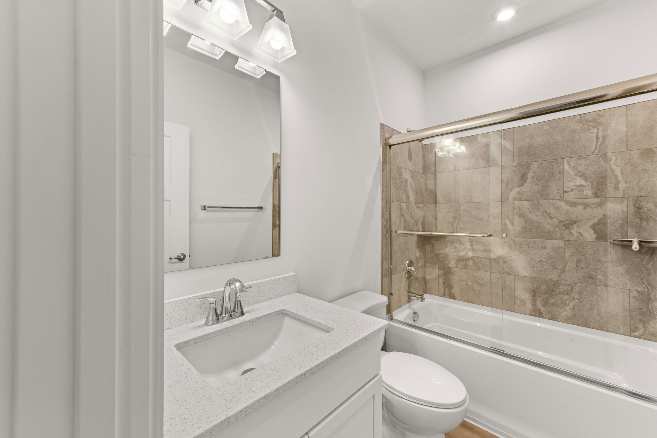 Modern bathroom with a white vanity, quartz countertop, and tiled bathtub-shower combo with glass doors.