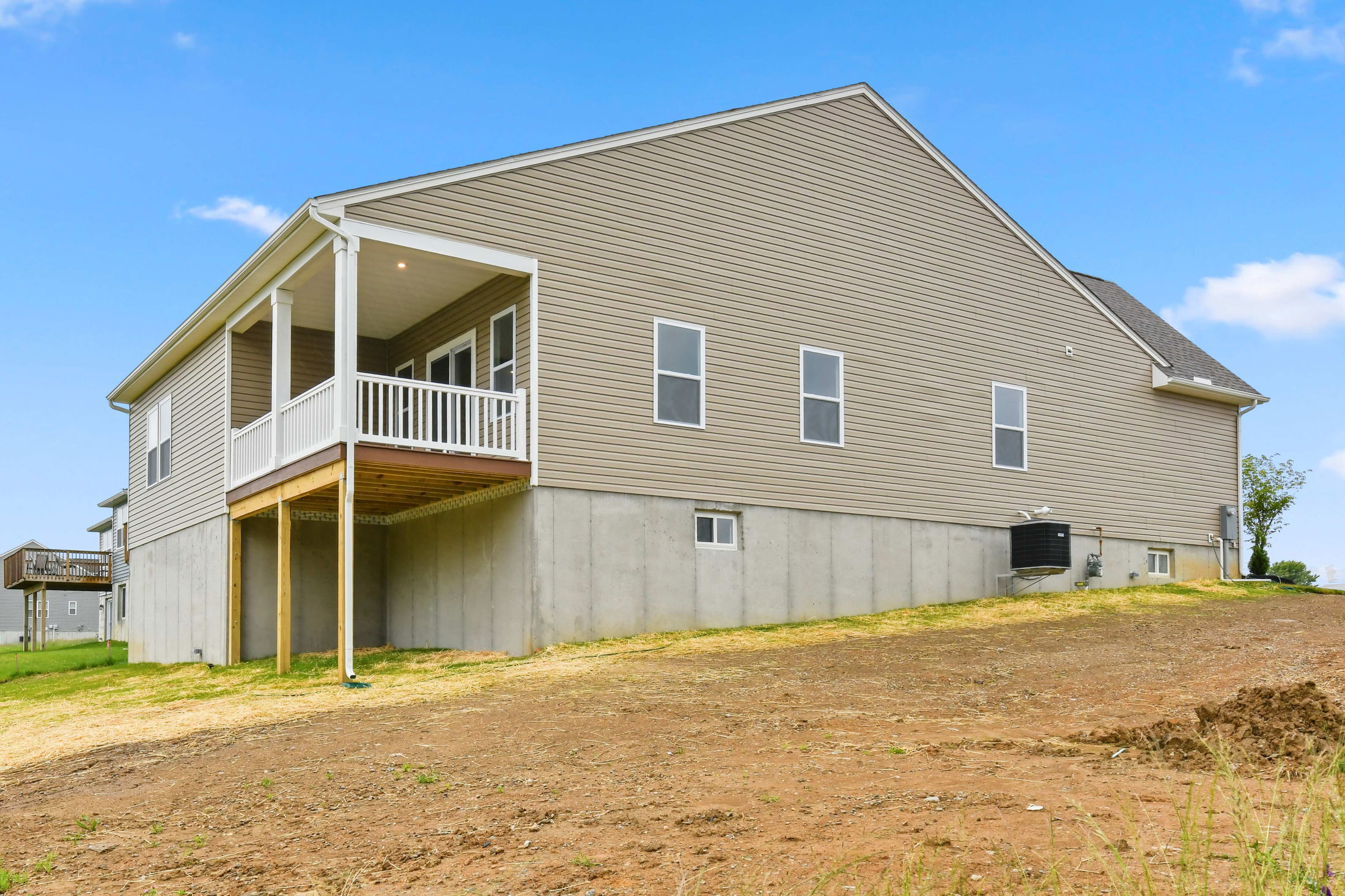 A modern beige house with a raised porch and sloped backyard under a clear blue sky.