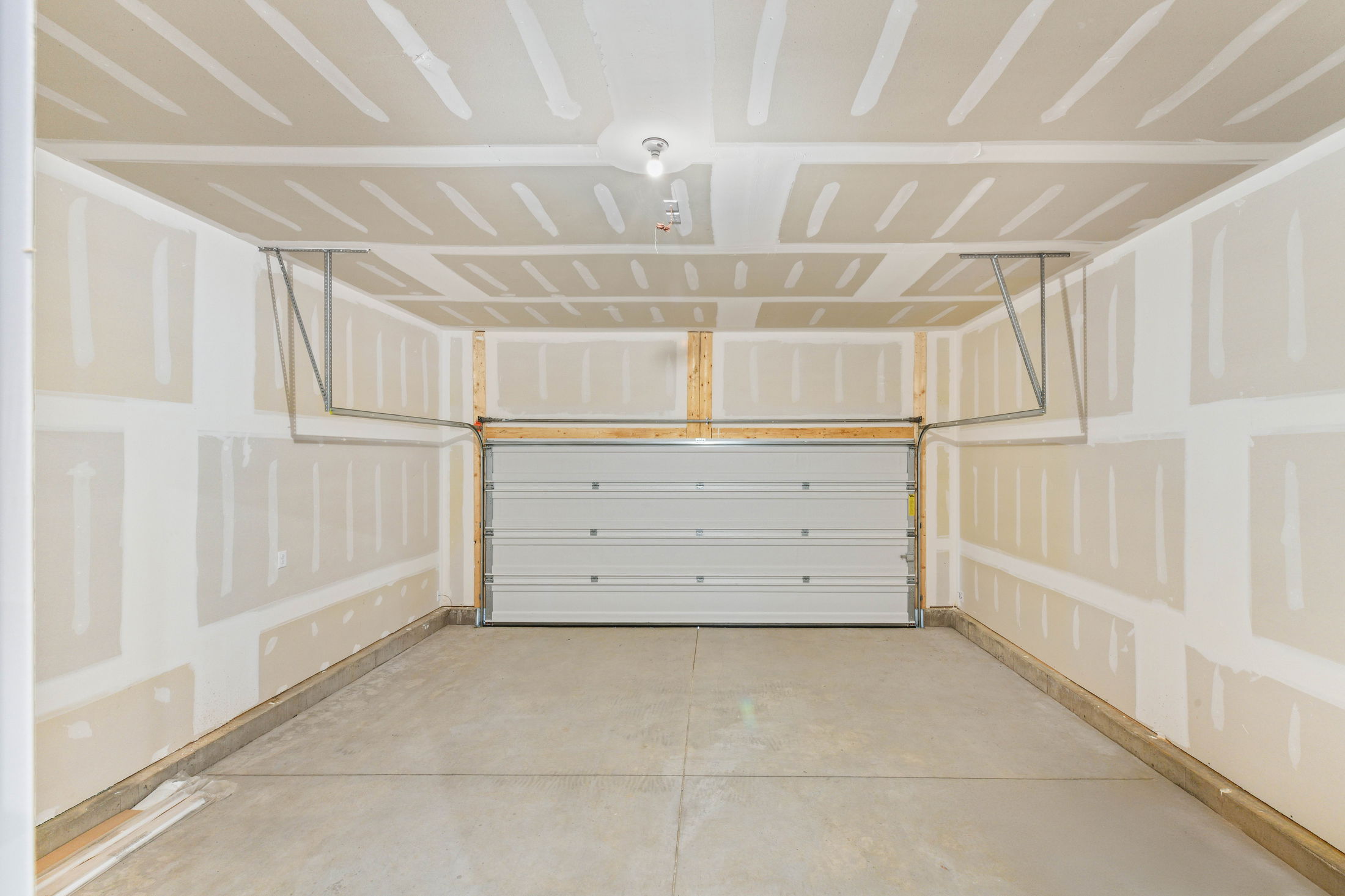 Empty garage interior with unfinished drywall and closed roll-up door.