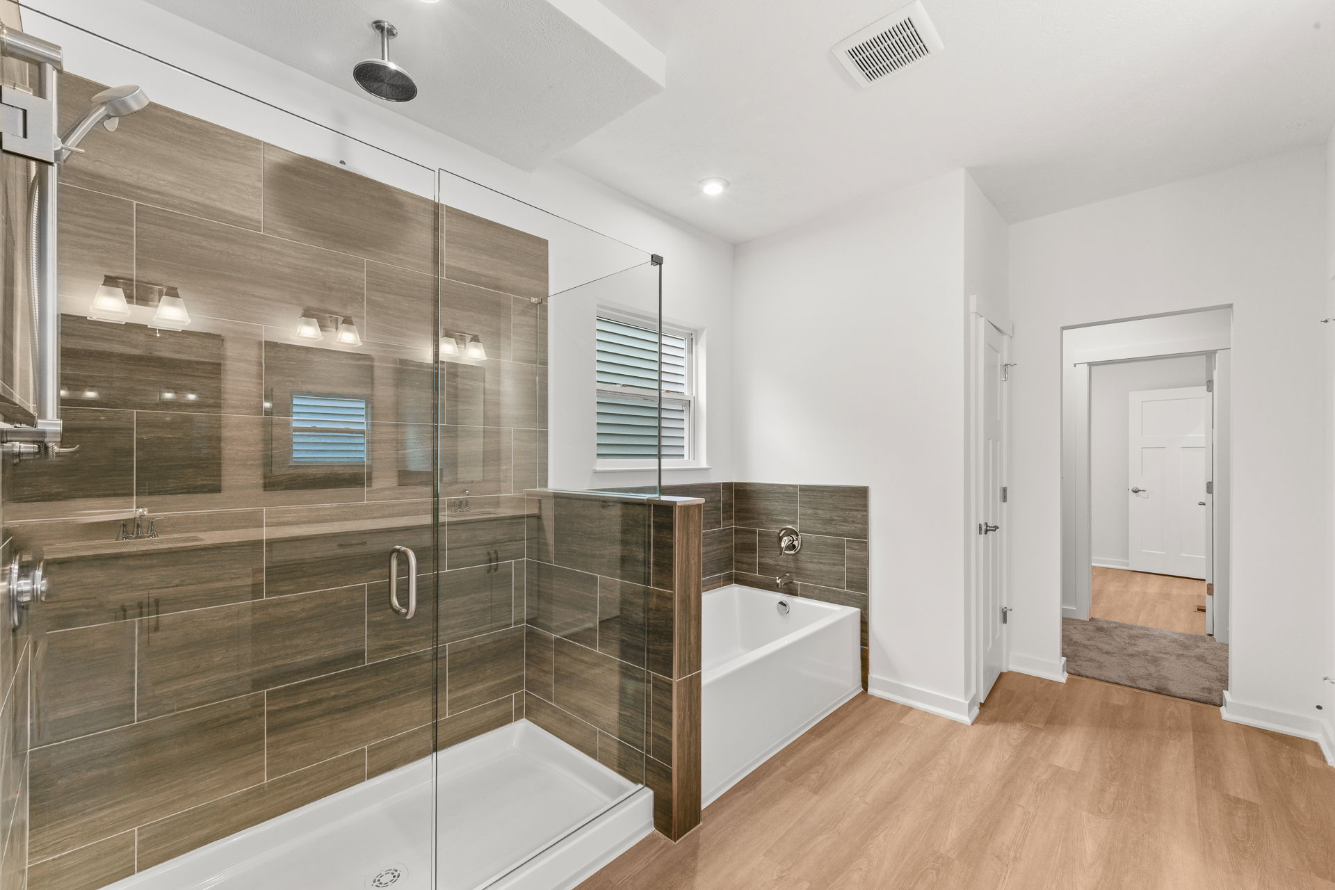 Modern bathroom with a glass-enclosed shower, bathtub, wood-style flooring, and contemporary lighting fixtures.