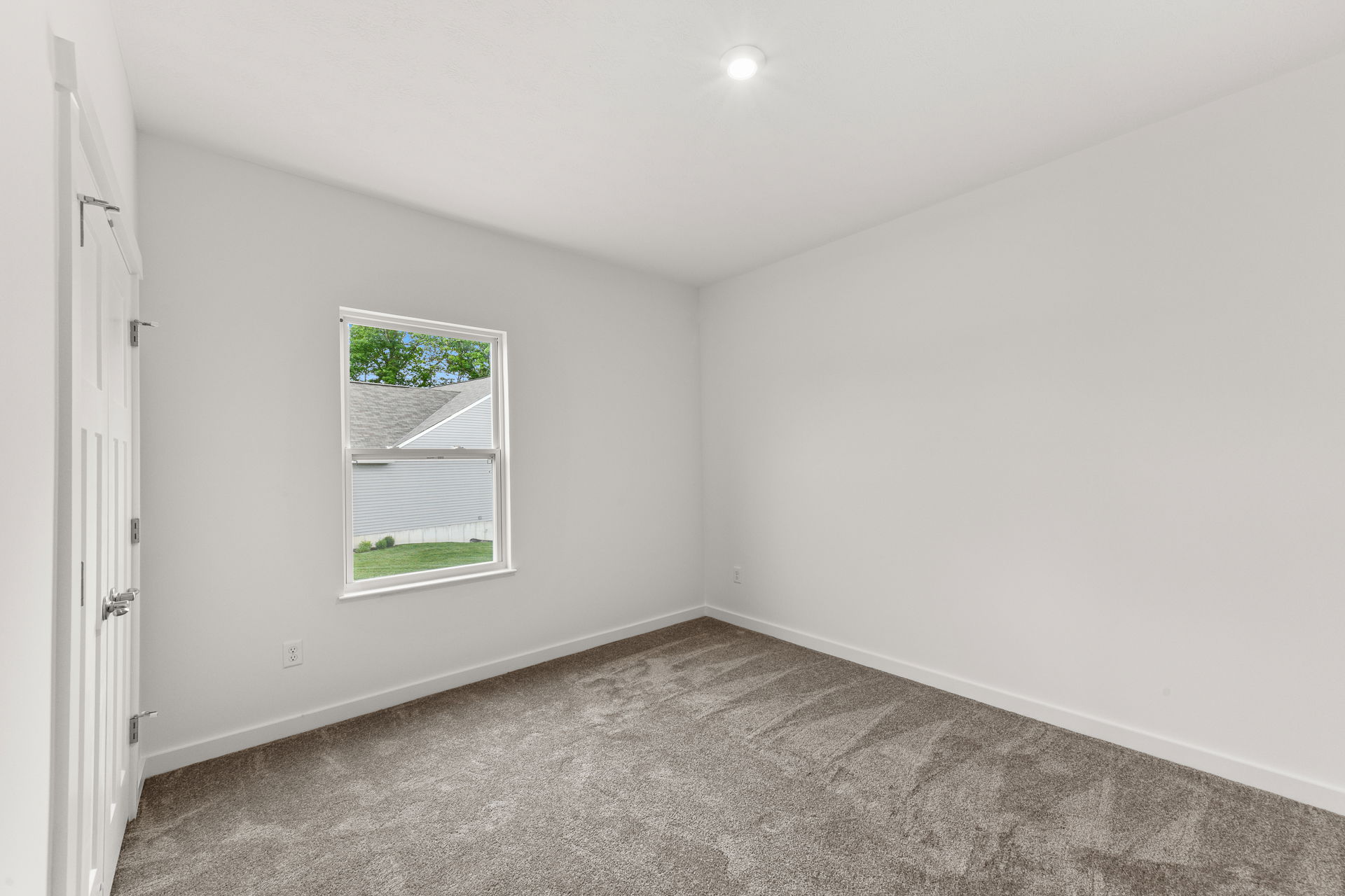 Empty white room with a single window and gray carpet, showcasing minimalist interior design.