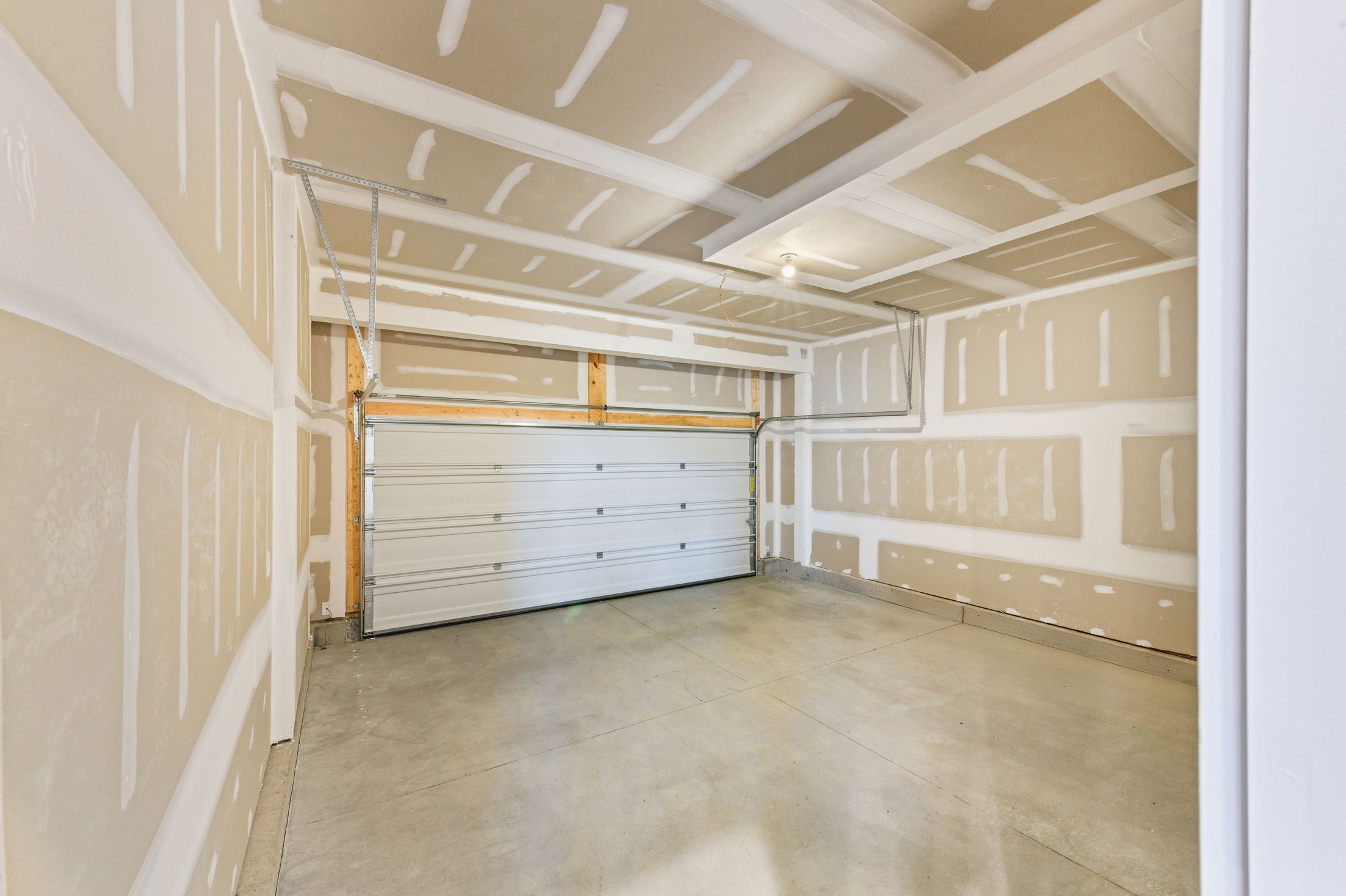 Empty two-car garage with unfinished drywall and an overhead door.