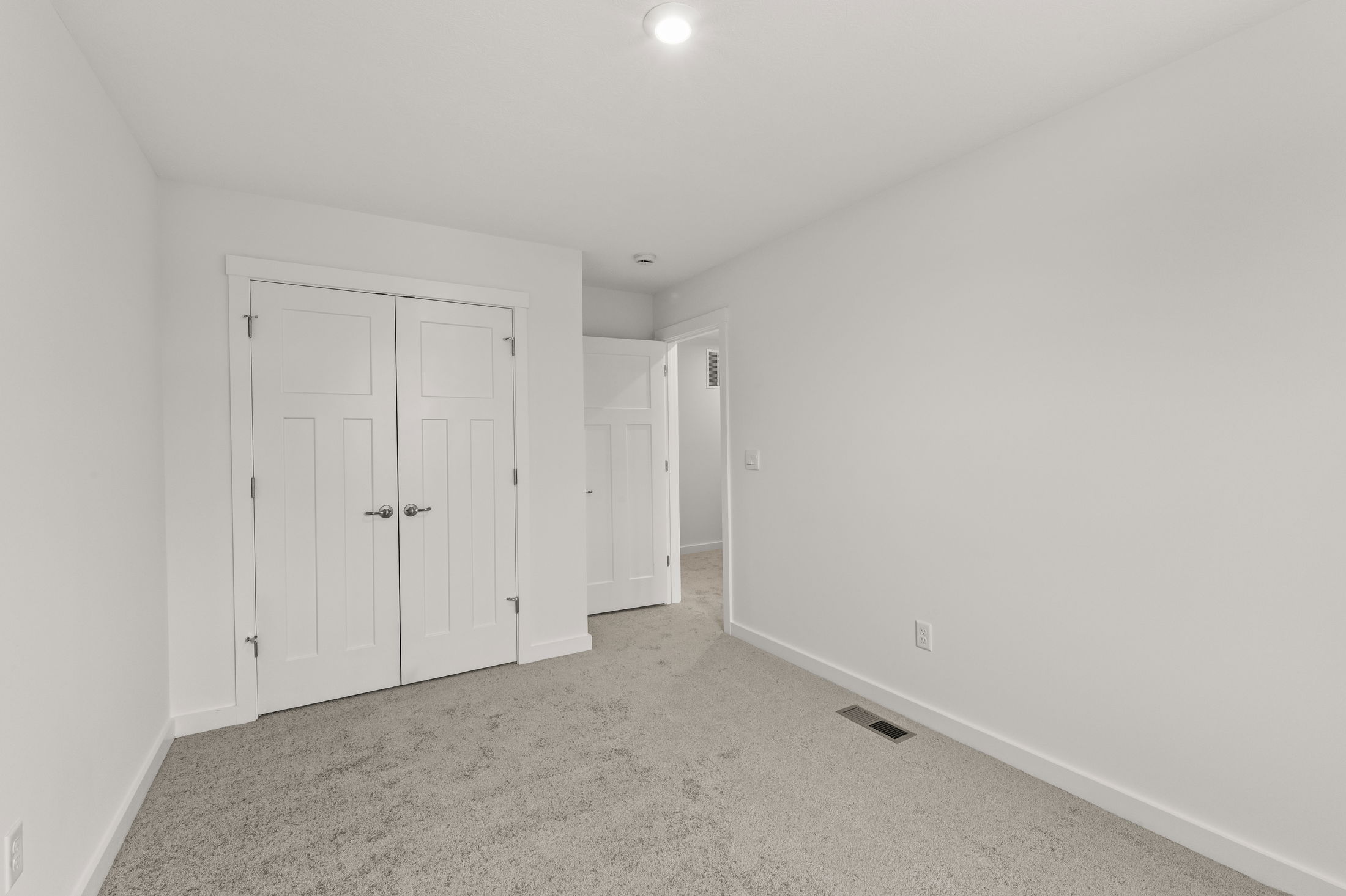 Minimalist empty room with beige carpet and a white double closet door.