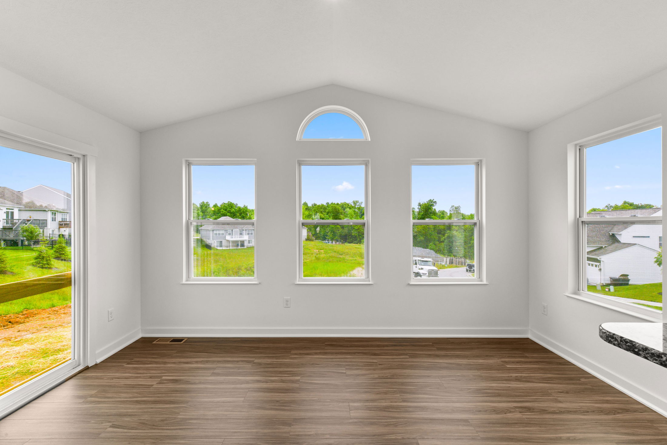 Bright, empty room with large windows overlooking a suburban neighborhood.