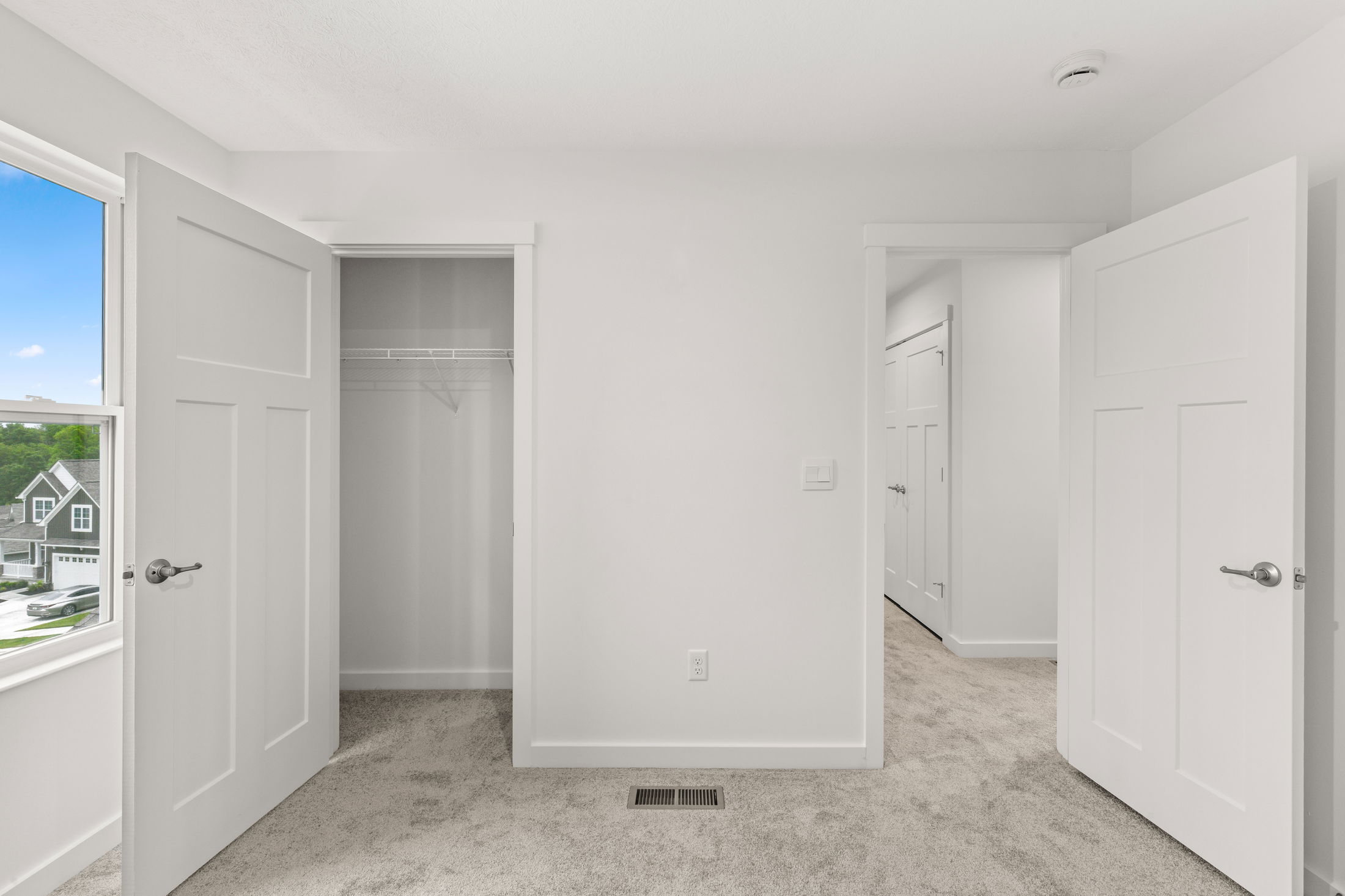 Empty white room featuring an open closet, two white doors, and a window with a view of neighboring houses.