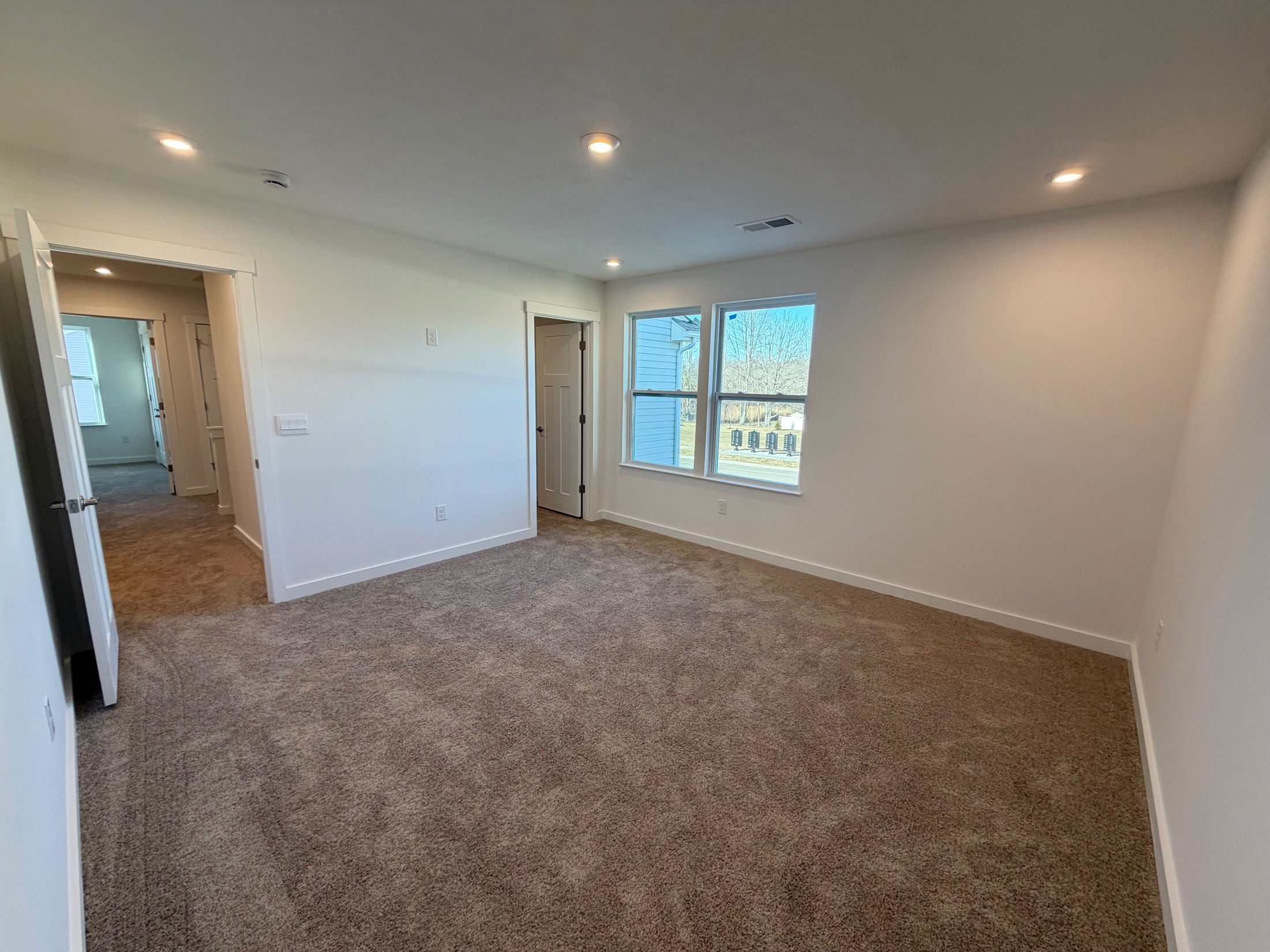 Spacious, well-lit bedroom with plush carpeting and large windows for natural light.
