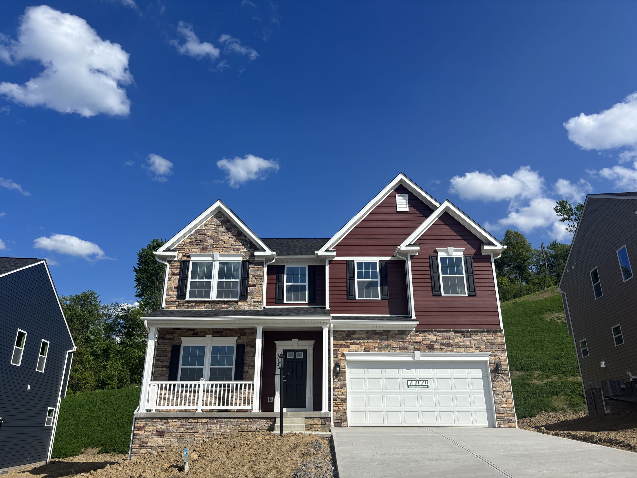 Two-story modern house with stone and red siding, large windows, and an attached garage under a clear blue sky.