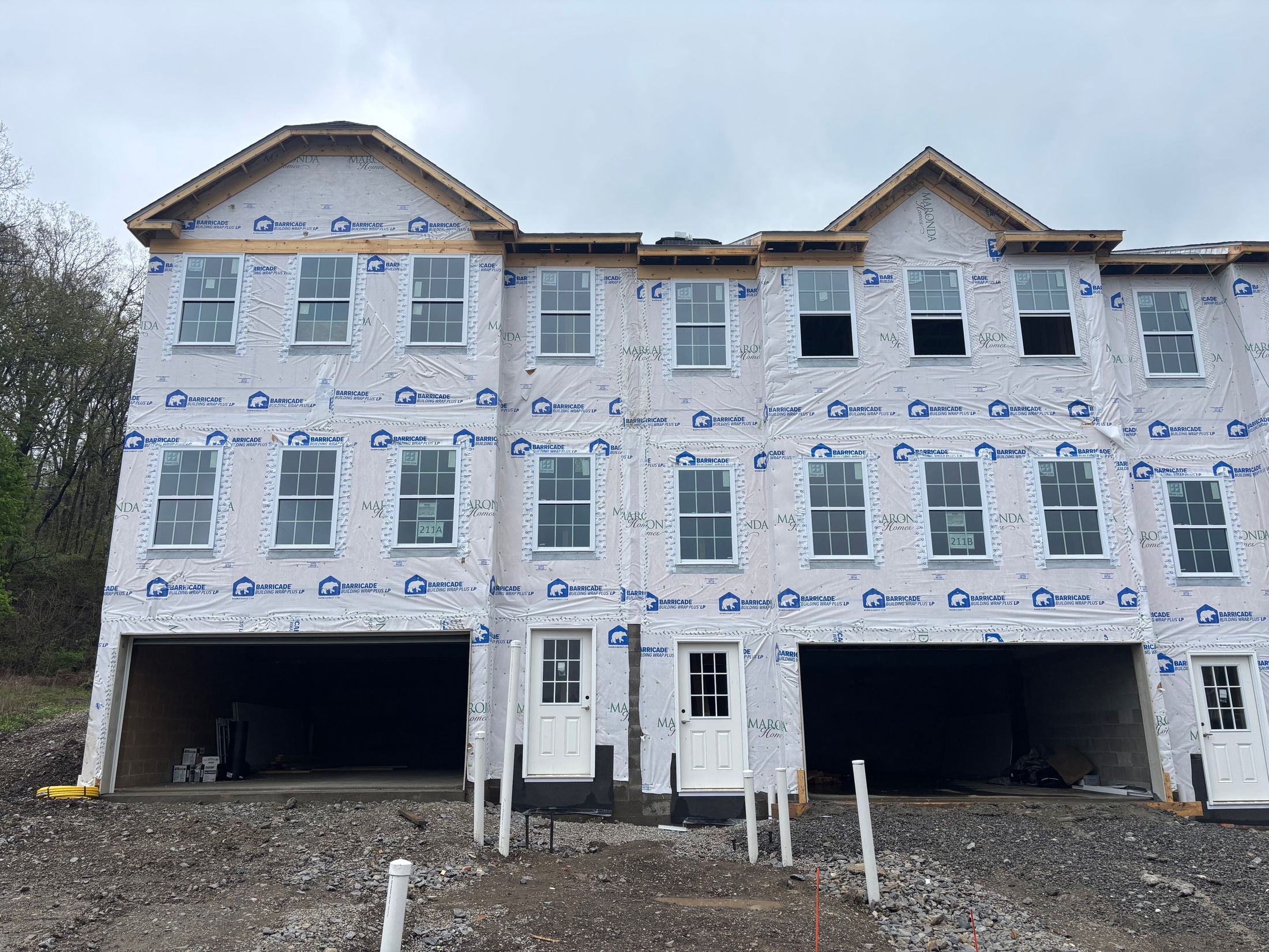 Newly constructed townhouse complex with visible protective wrap and garage spaces.