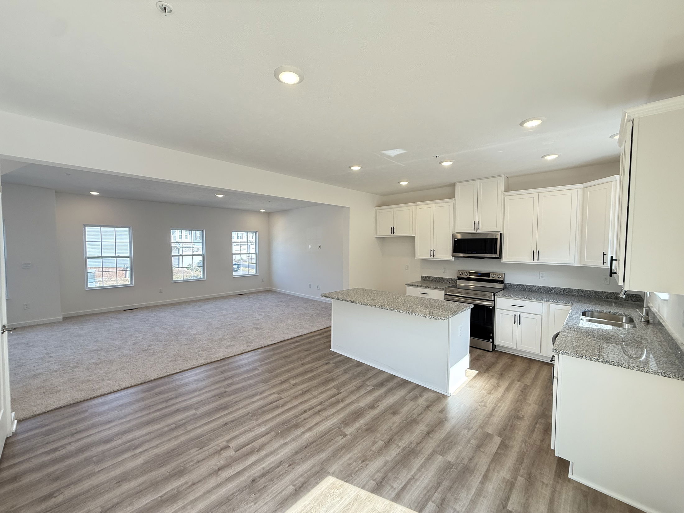 Spacious open-concept kitchen and living room with hardwood floors, modern white cabinets, and granite countertops.