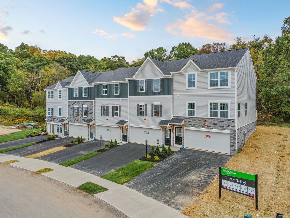 A row of newly constructed, modern multi-story townhouses in a residential development surrounded by trees, with a 