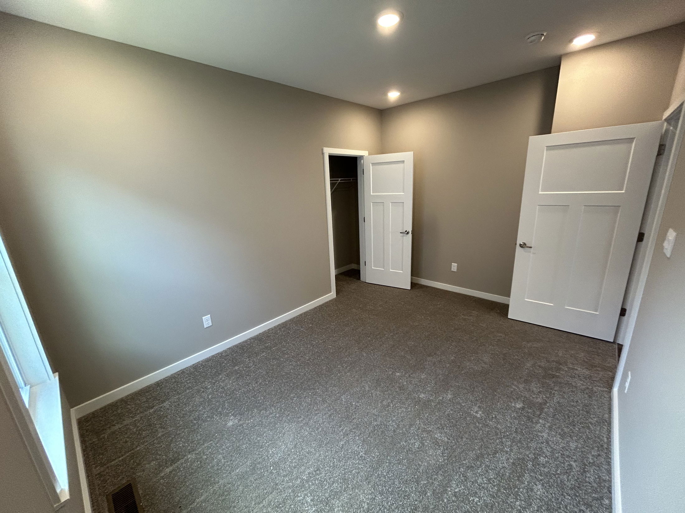 Empty carpeted room with beige walls, recessed lighting, open closet, and two white doors.