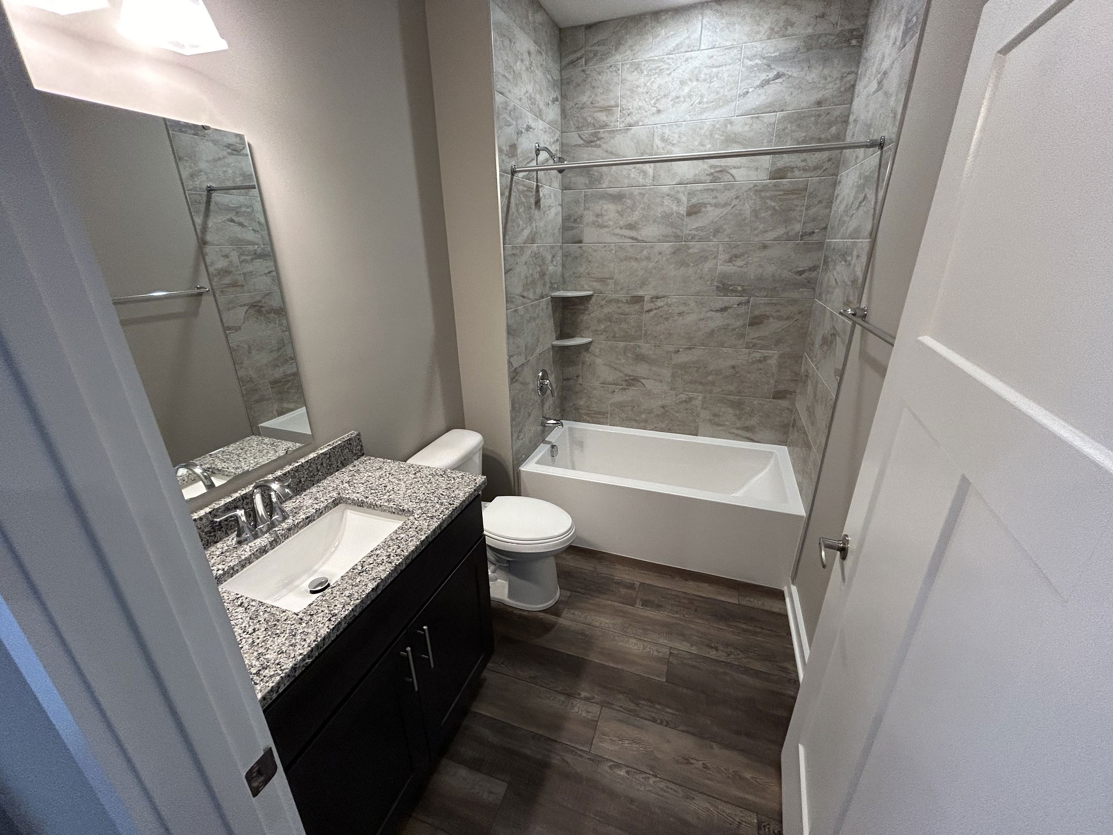 Modern bathroom with granite countertop, dark vanity, and tiled bathtub shower combination.