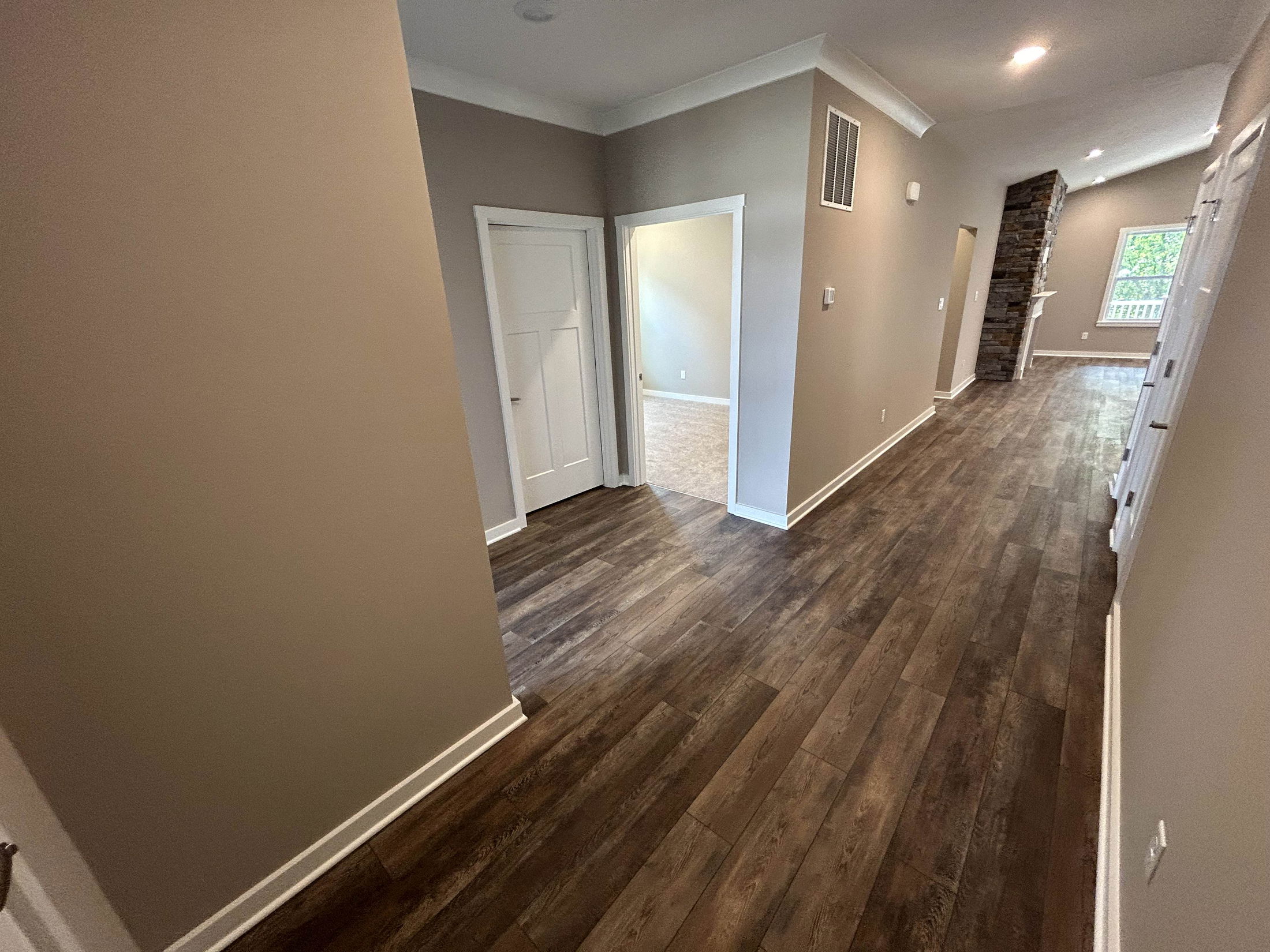 Modern interior hallway with dark wood flooring, neutral walls, and recessed lighting leading to a stone fireplace.